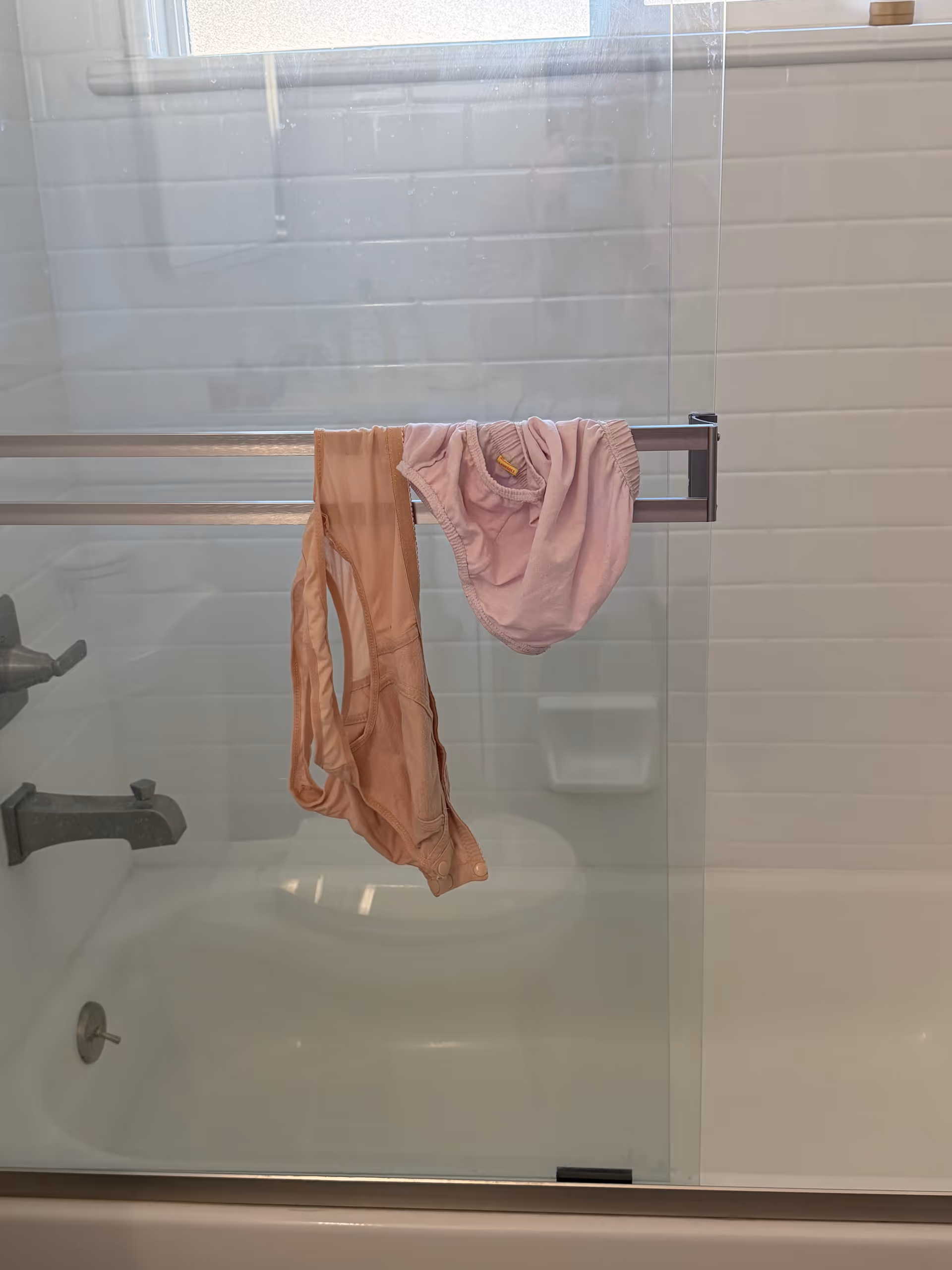 Shower with glass door, tiled walls, and pink garments draped over a rack.