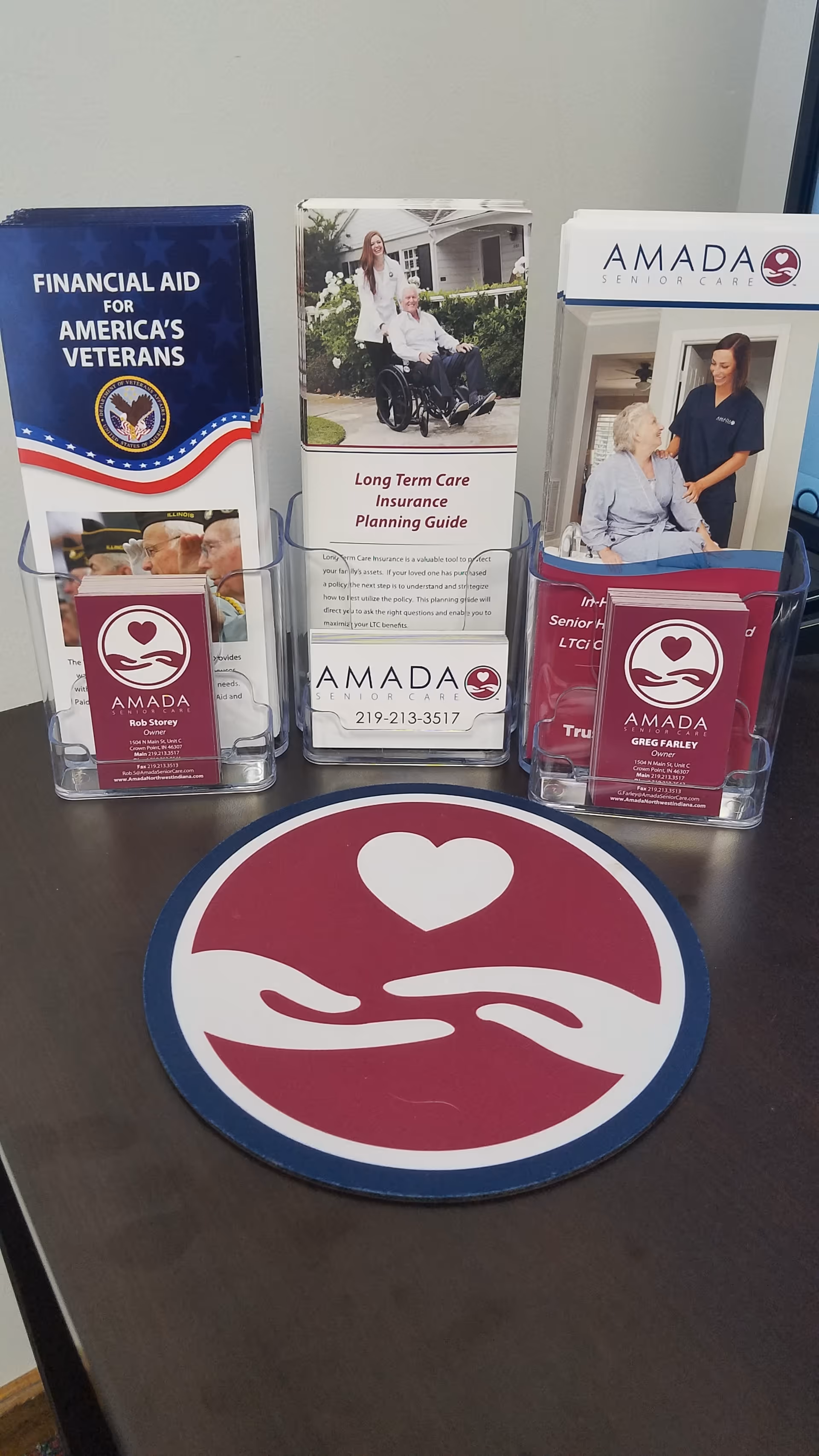 Three brochure displays and a heart-hand logo on a table at Amada Senior Care.