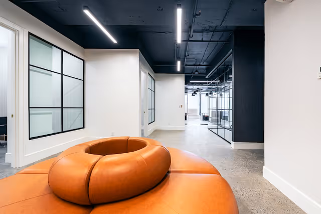 Modern interior lobby with curved orange seating, glass partitions, and white walls.