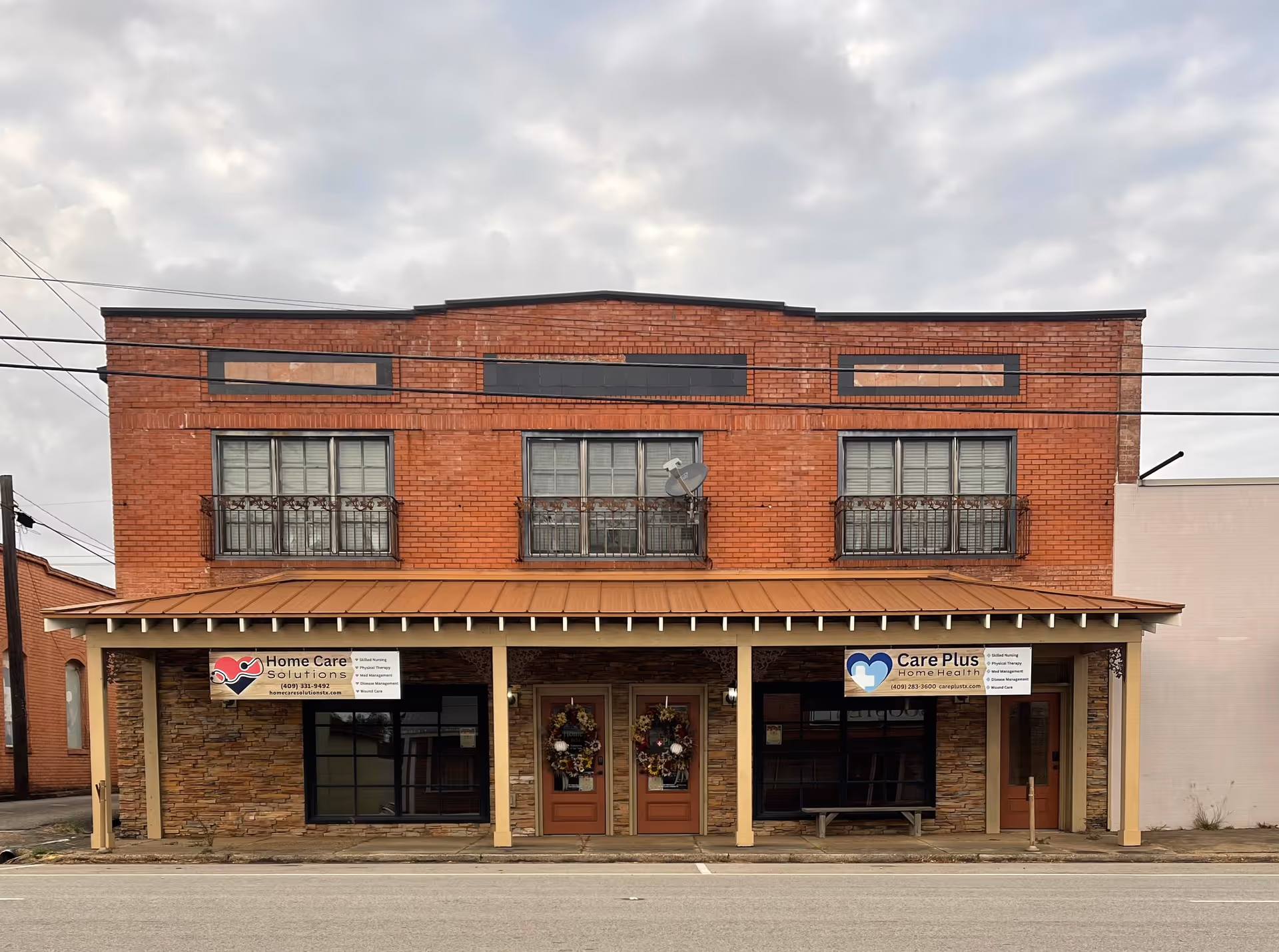 A brick two-story building storefront houses Care Plus Home Health with double entry doors and banners.