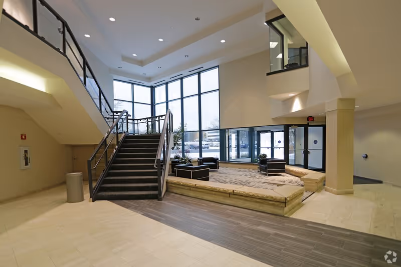 Spacious modern senior-living lobby featuring a staircase, seating pods, and expansive floor-to-ceiling windows.