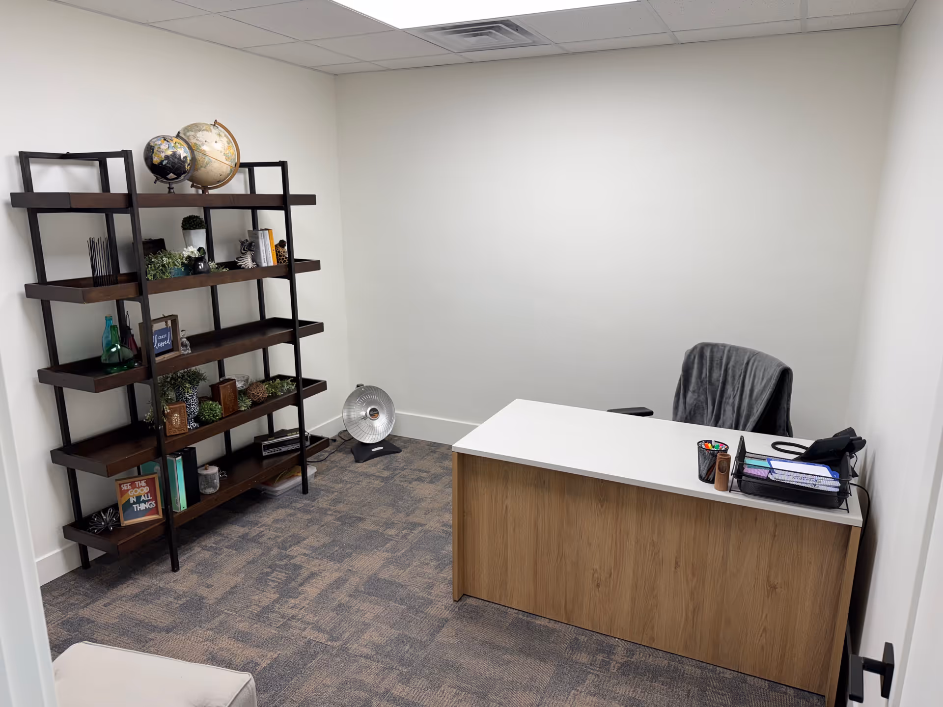 A small office in a senior living facility with desk, chair, and metal bookshelf.