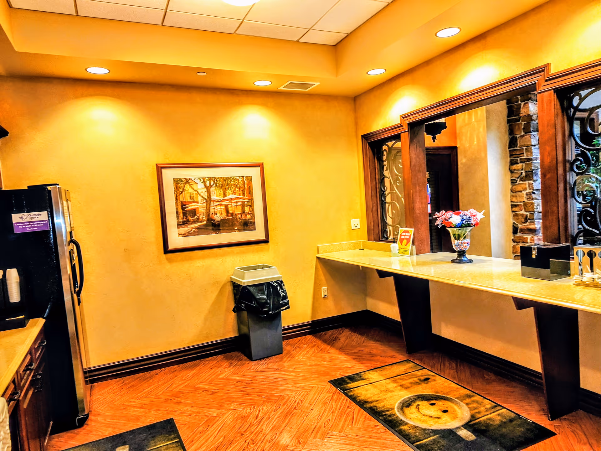 Warm, well-lit lobby area with a long counter, artwork, and a trash receptacle.