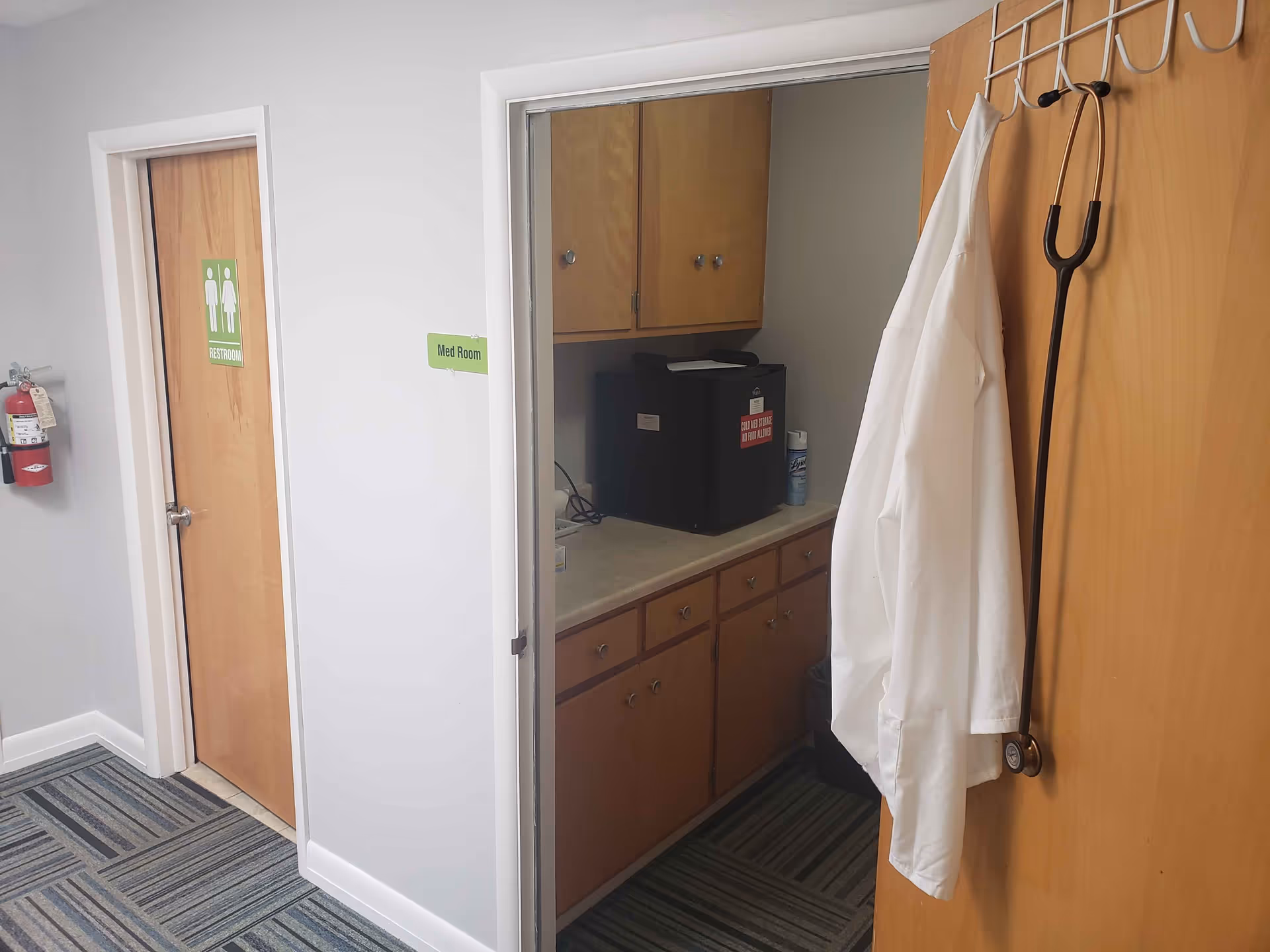 Interior of a facility corridor showing a med room, cabinets, and a hanging coat.