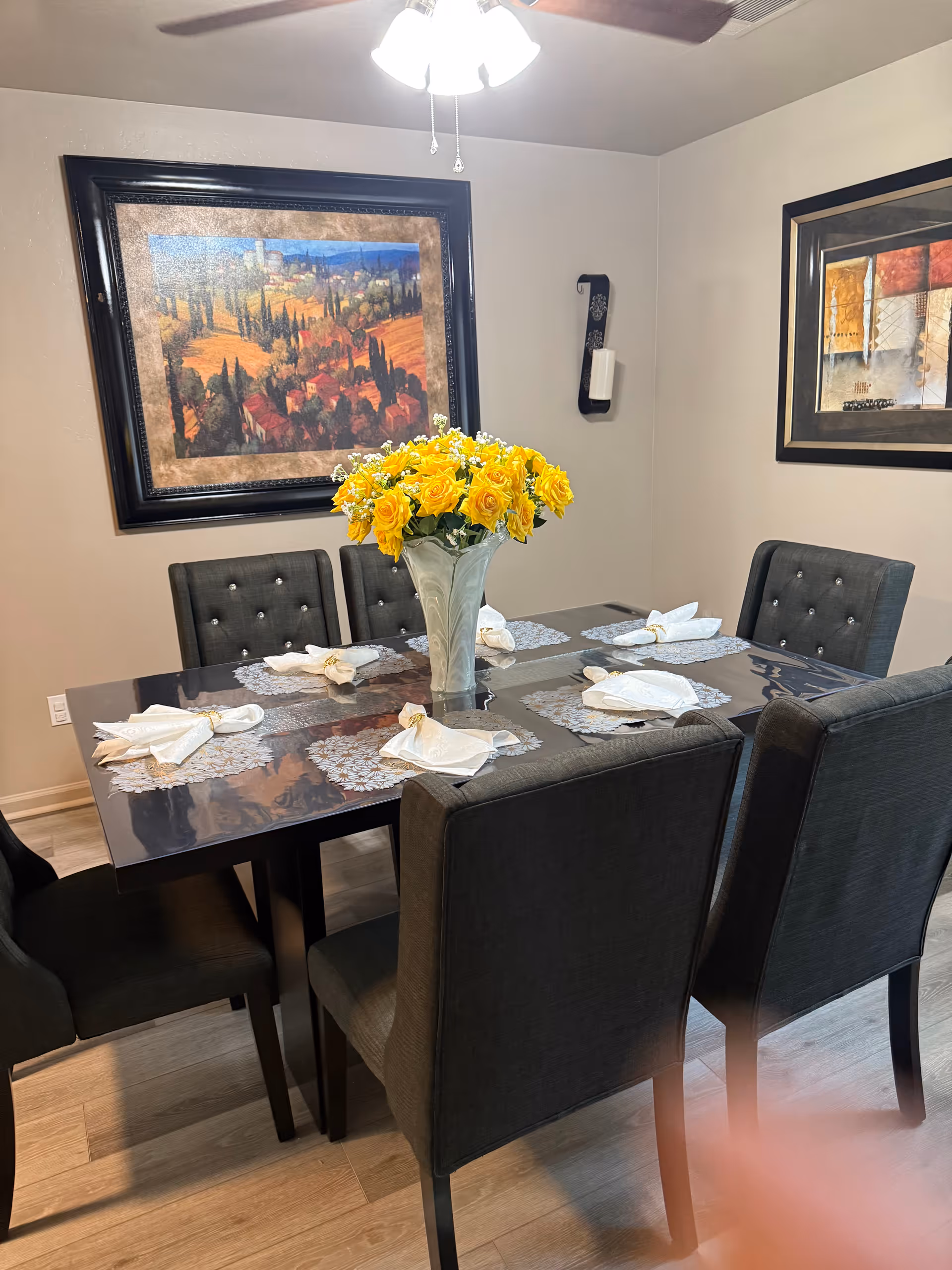 Dark dining table with yellow flower centerpiece and folded napkins in a dining room.