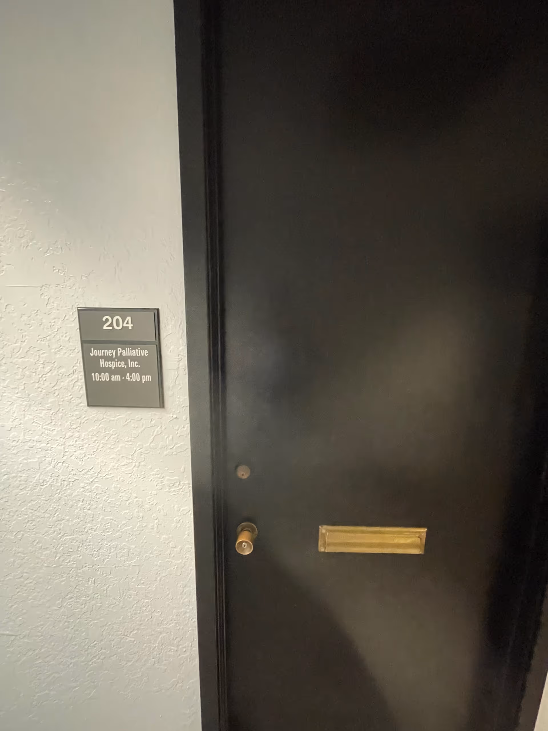 Dark interior door with a gold mail slot and plaque for room 204, Journey Palliative Hospice.