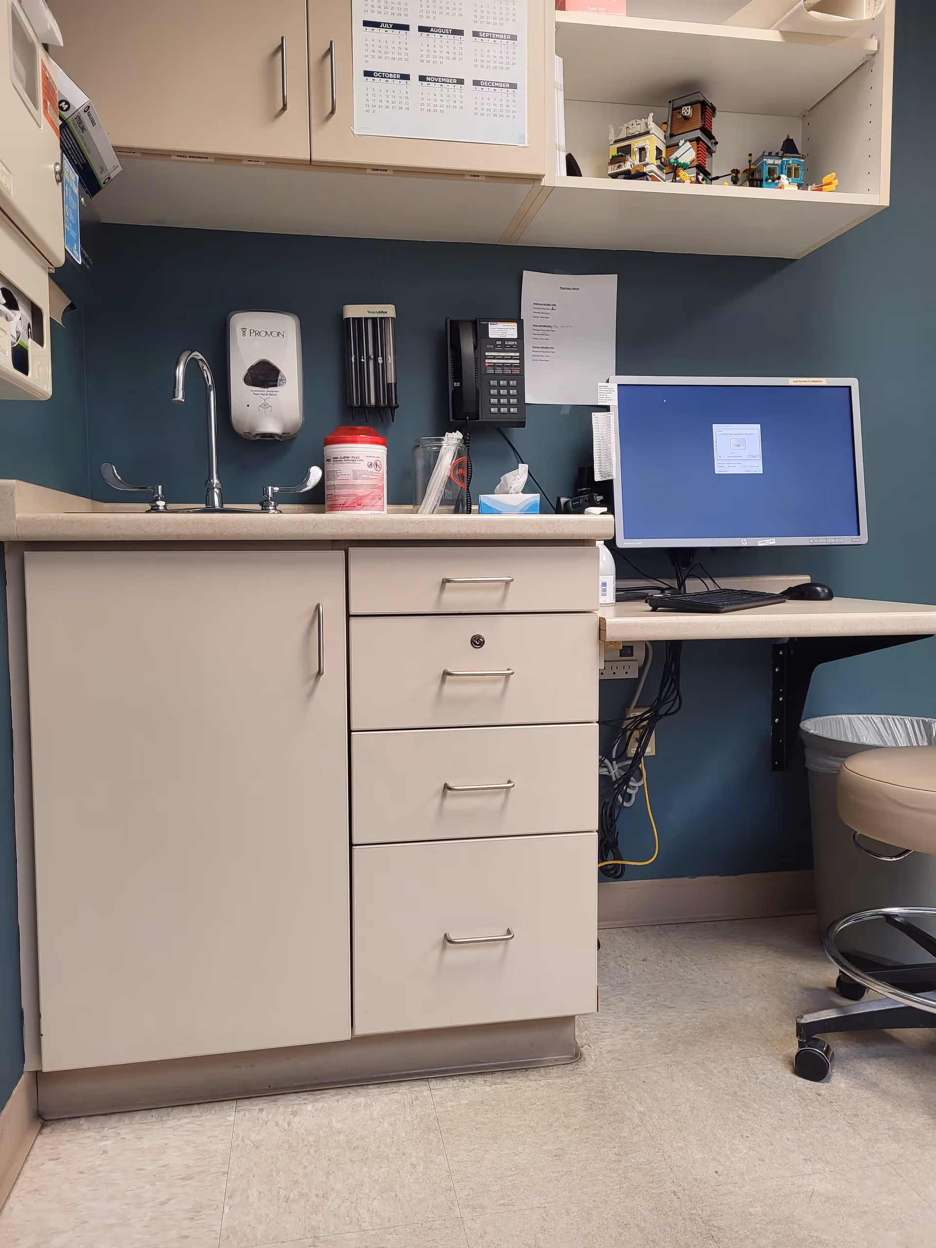 A clinic workstation with a sink, cabinets, drawers, and a computer.