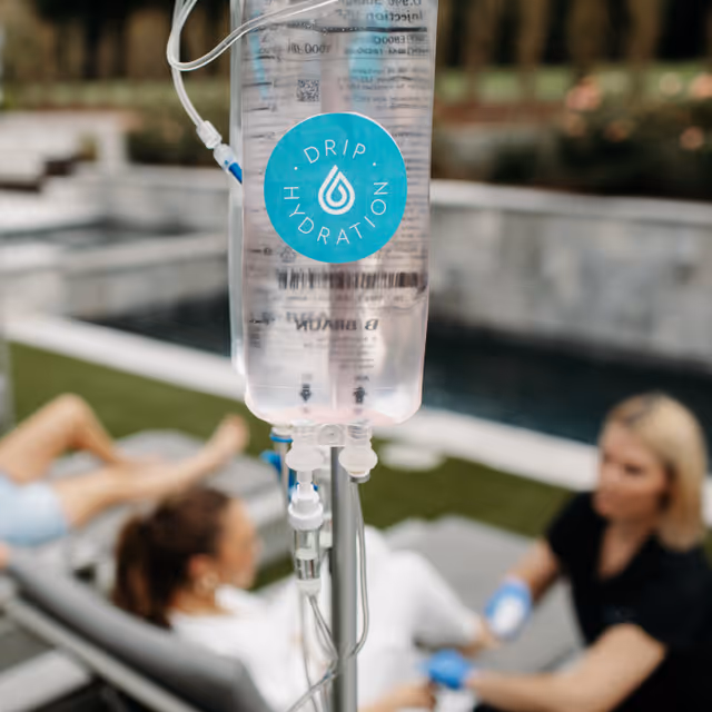 IV drip bag with Drip Hydration logo; poolside lounge blurred in background.