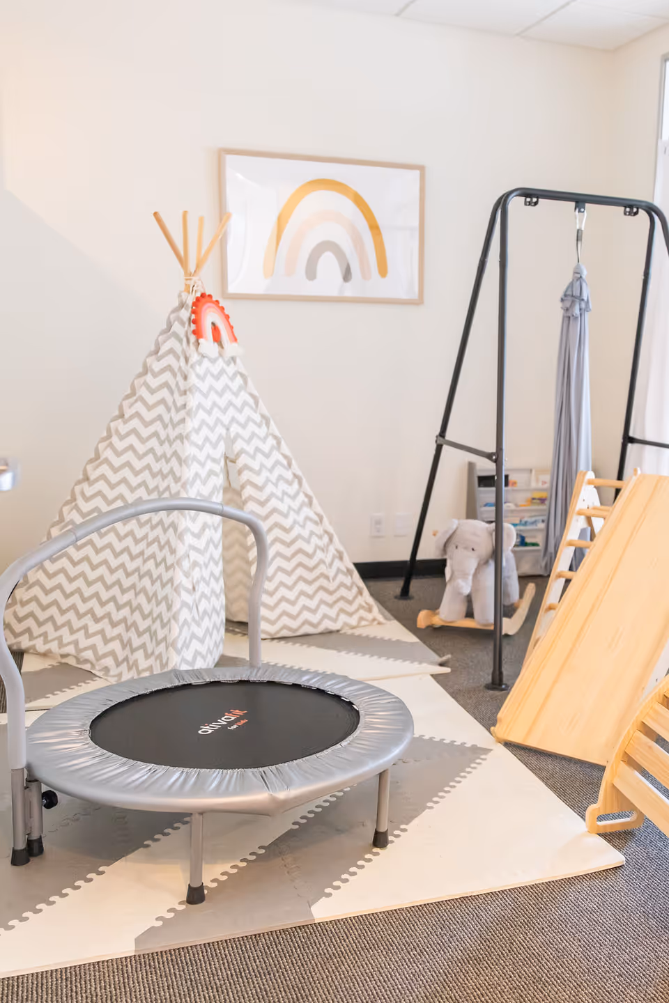 Bright indoor activity space with a mini trampoline, tipi tent, climbing frame, and slide.