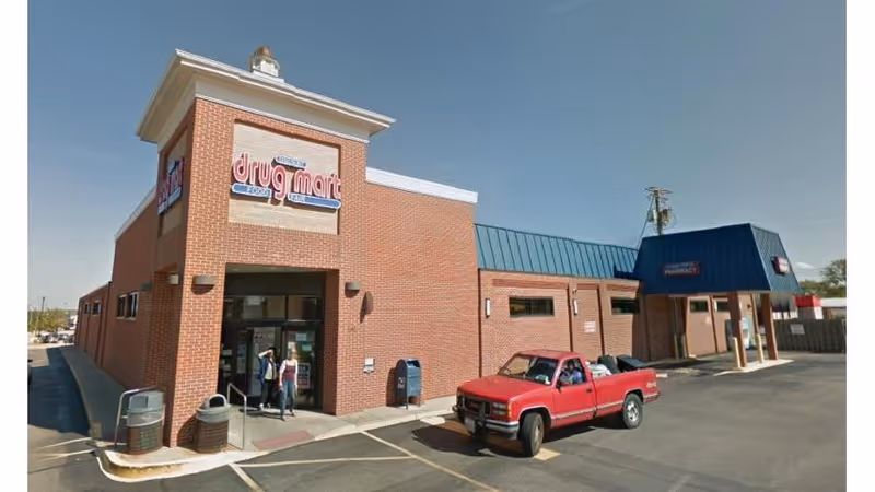 Brick Discount Drug Mart storefront with a blue awning and a red pickup truck in front.