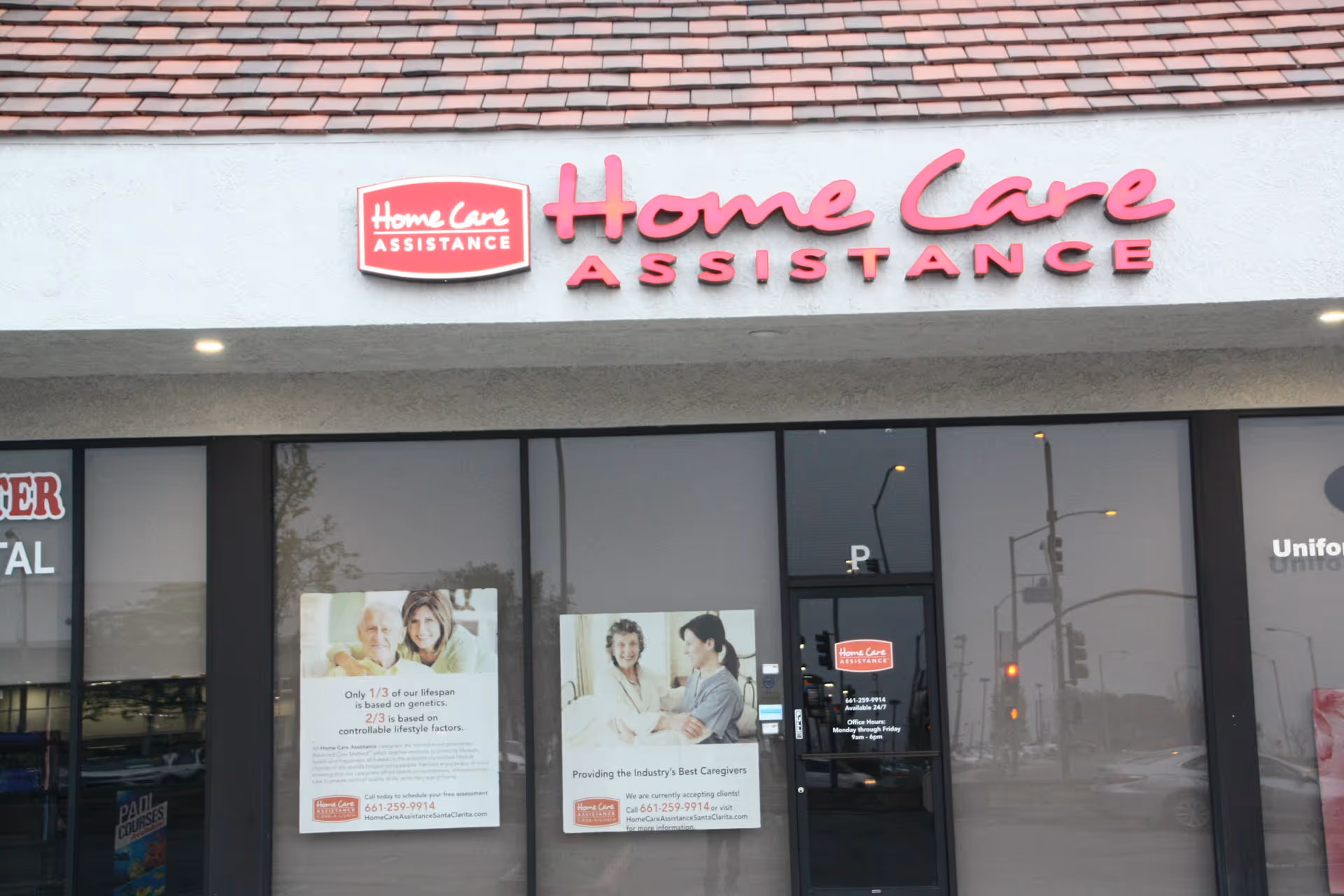 Exterior storefront with large pink Home Care Assistance sign and posters in windows.