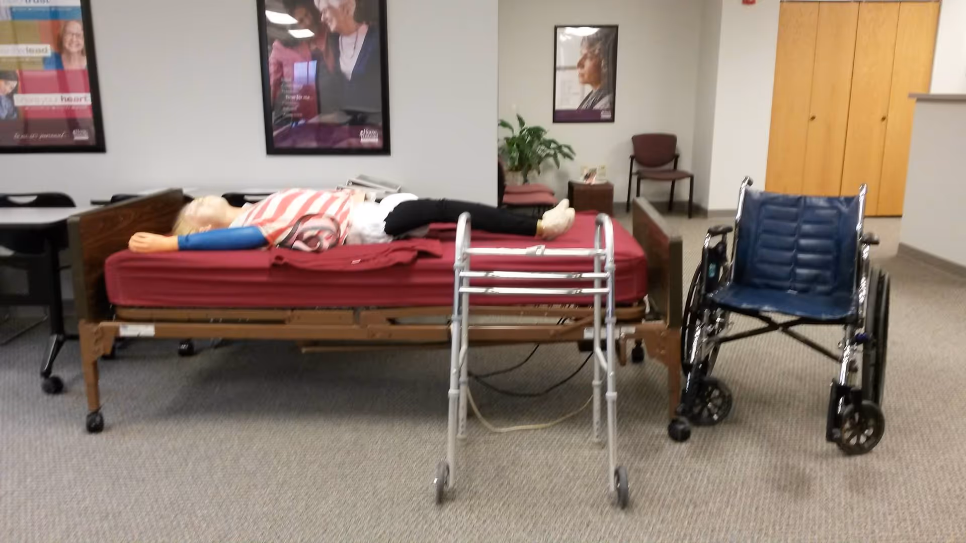 A person lying on a hospital bed with a walker and wheelchair in a care facility.