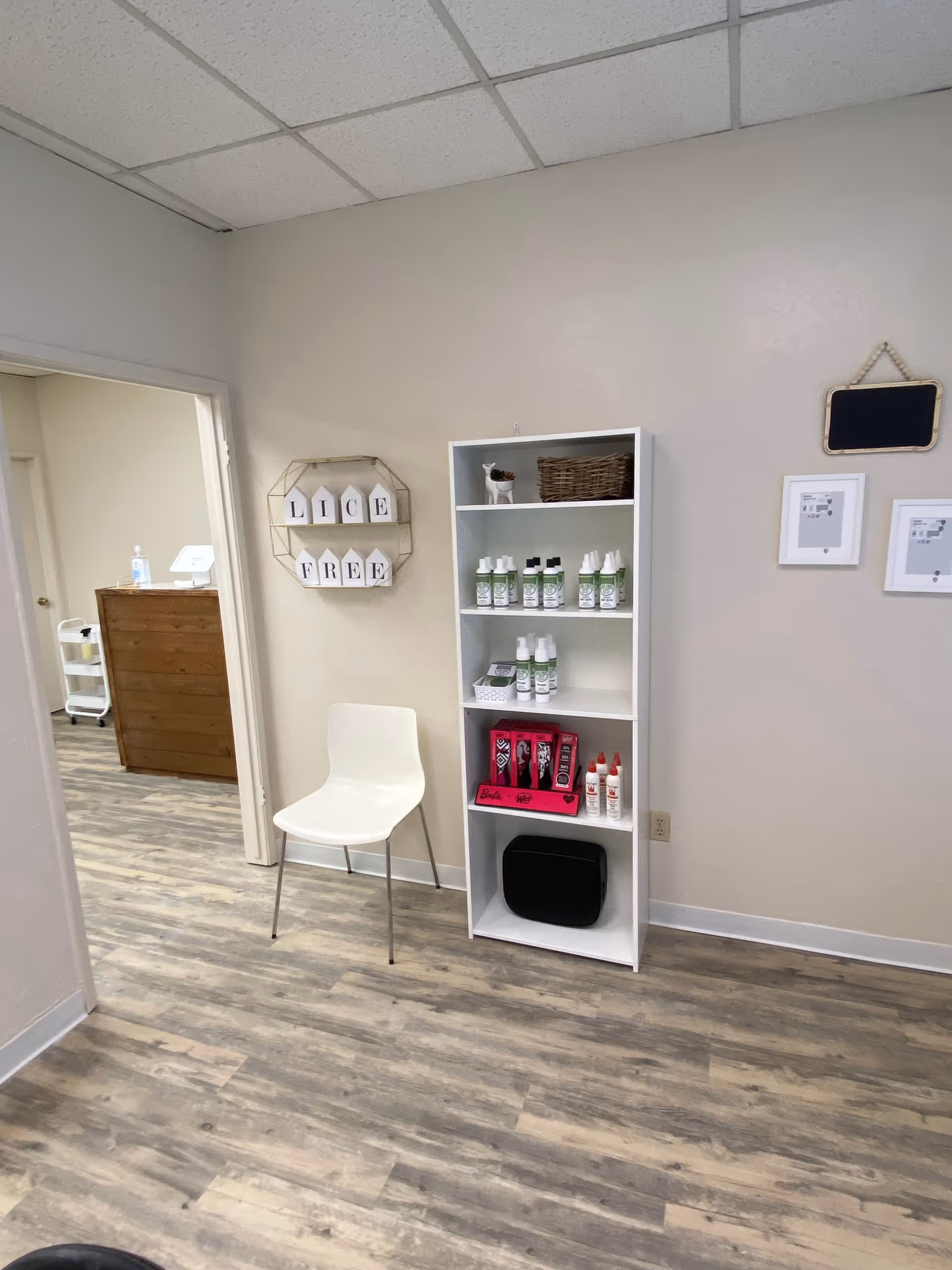 A clean, small treatment room with a white chair and a shelf of lice products.