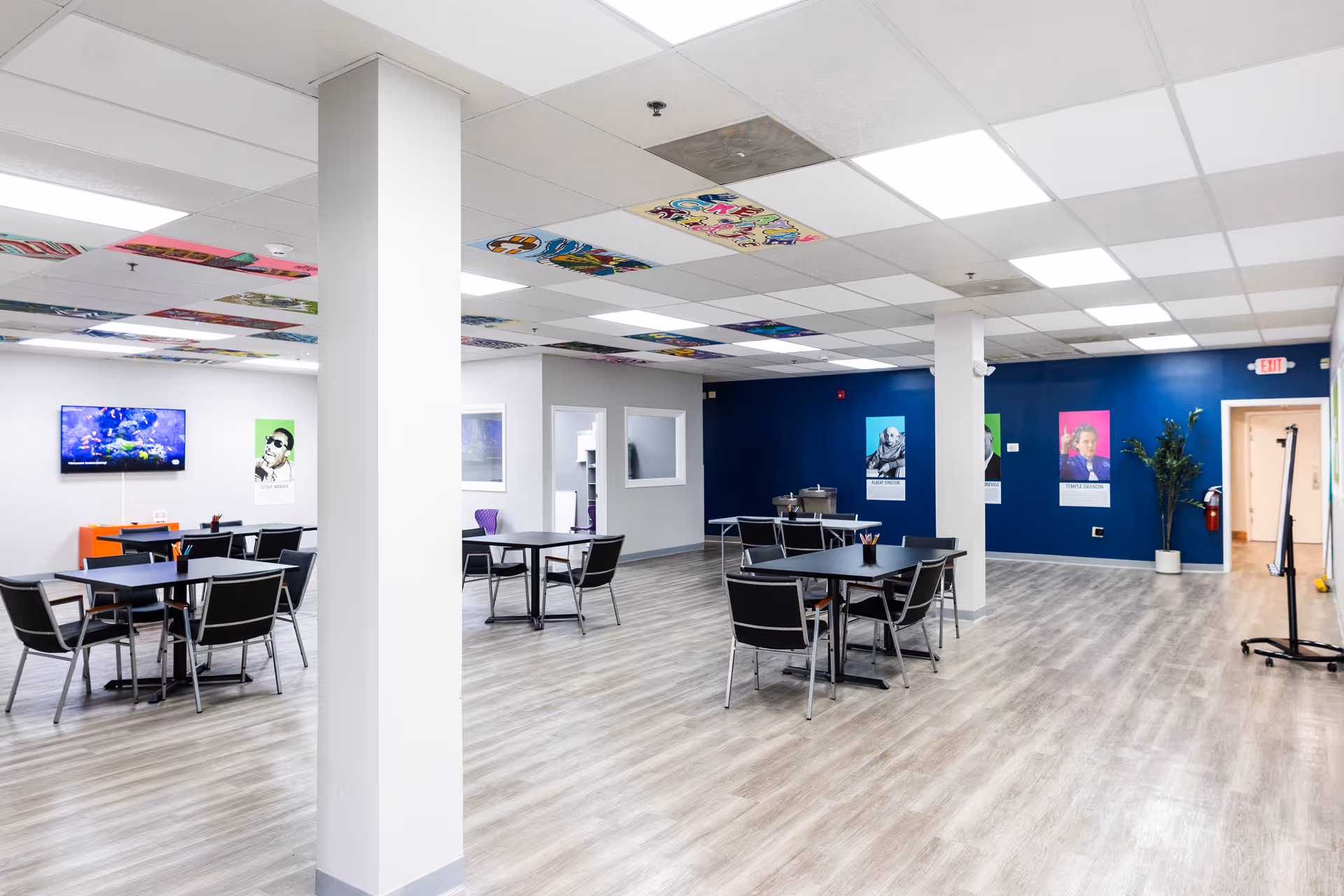 Bright open communal dining area with multiple tables and black chairs.