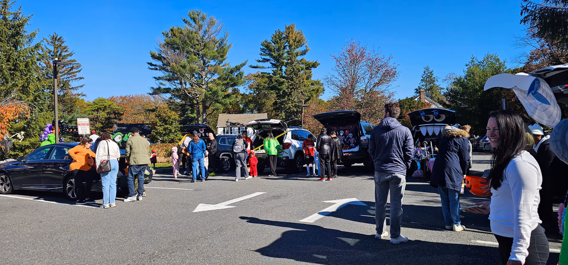 A crowded outdoor parking lot event with people gathered around open car trunks.