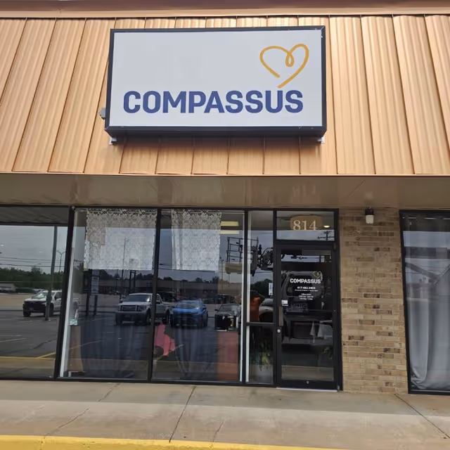 Exterior of a Compassus facility with sign above glass entry doors.
