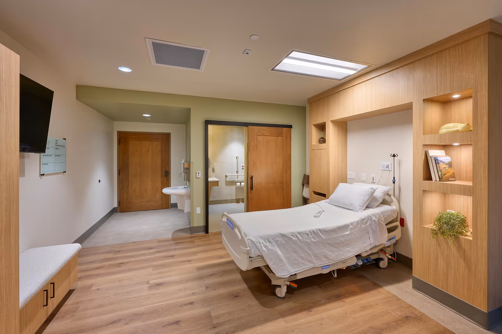 Hospice patient bedroom with adjustable bed, built-in shelves, and bathroom doorway.