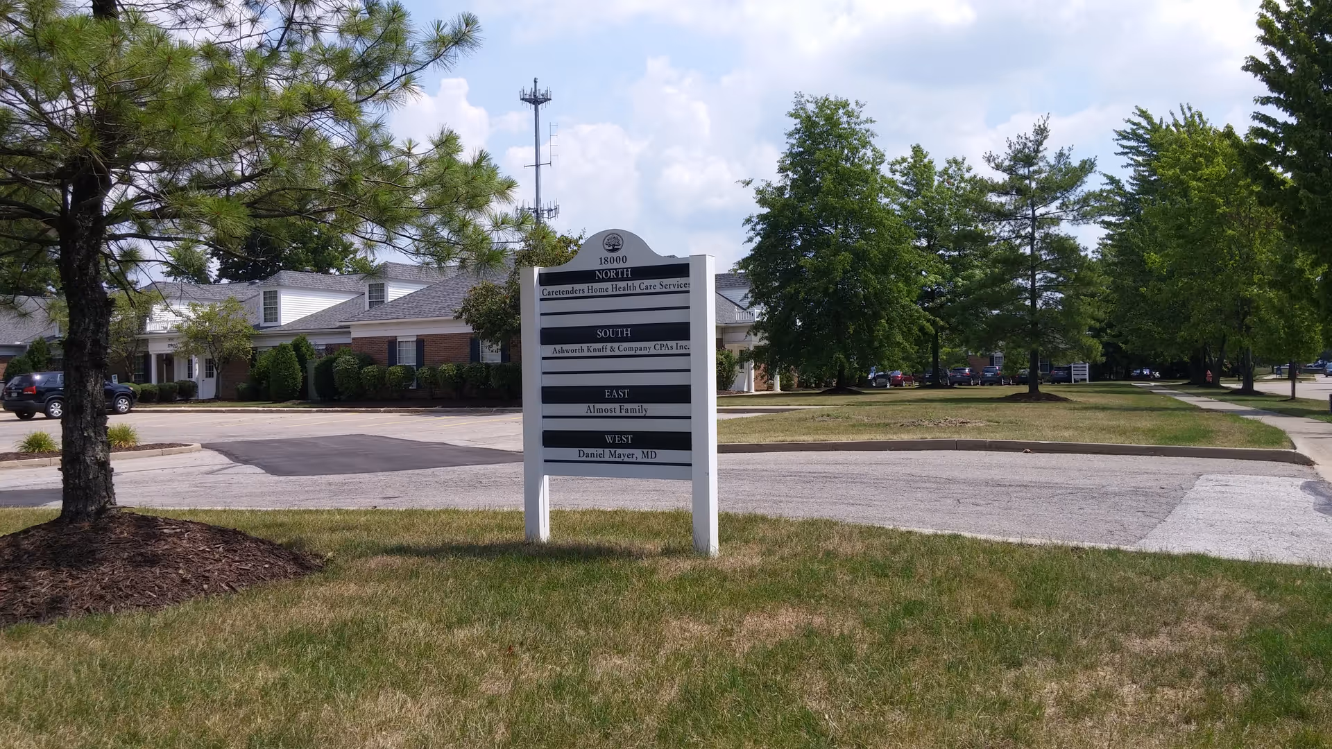 Exterior view of a senior living facility with a sign, trees, and a parking lot