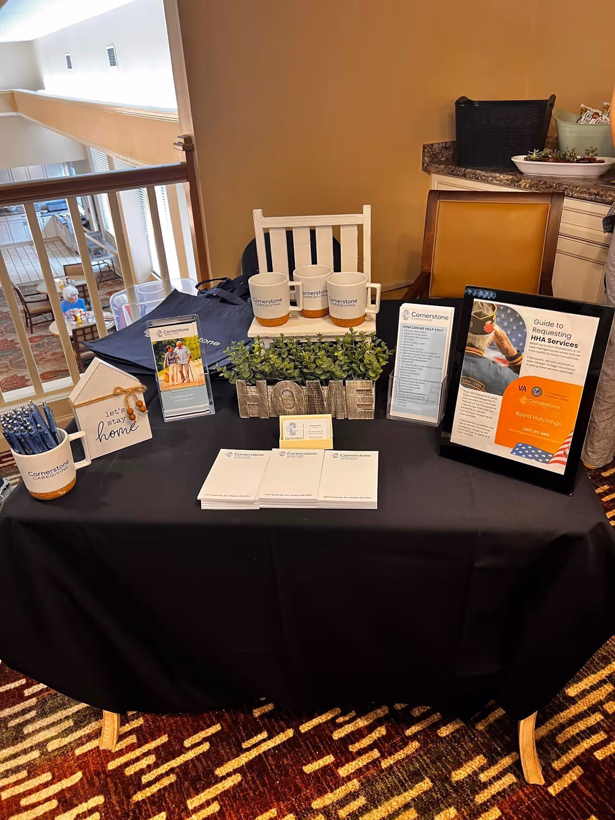 Promotional display table with brochures, mugs, plants, and Cornerstone Caregiving signage.
