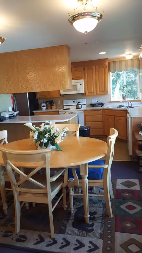 Round wooden dining table with floral centerpiece in a kitchen-adjacent dining area.