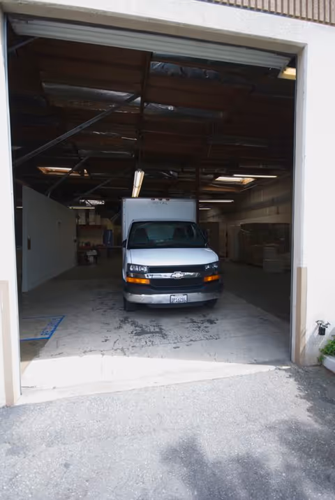 Open garage with a white Chevrolet cargo van parked inside a warehouse loading bay.