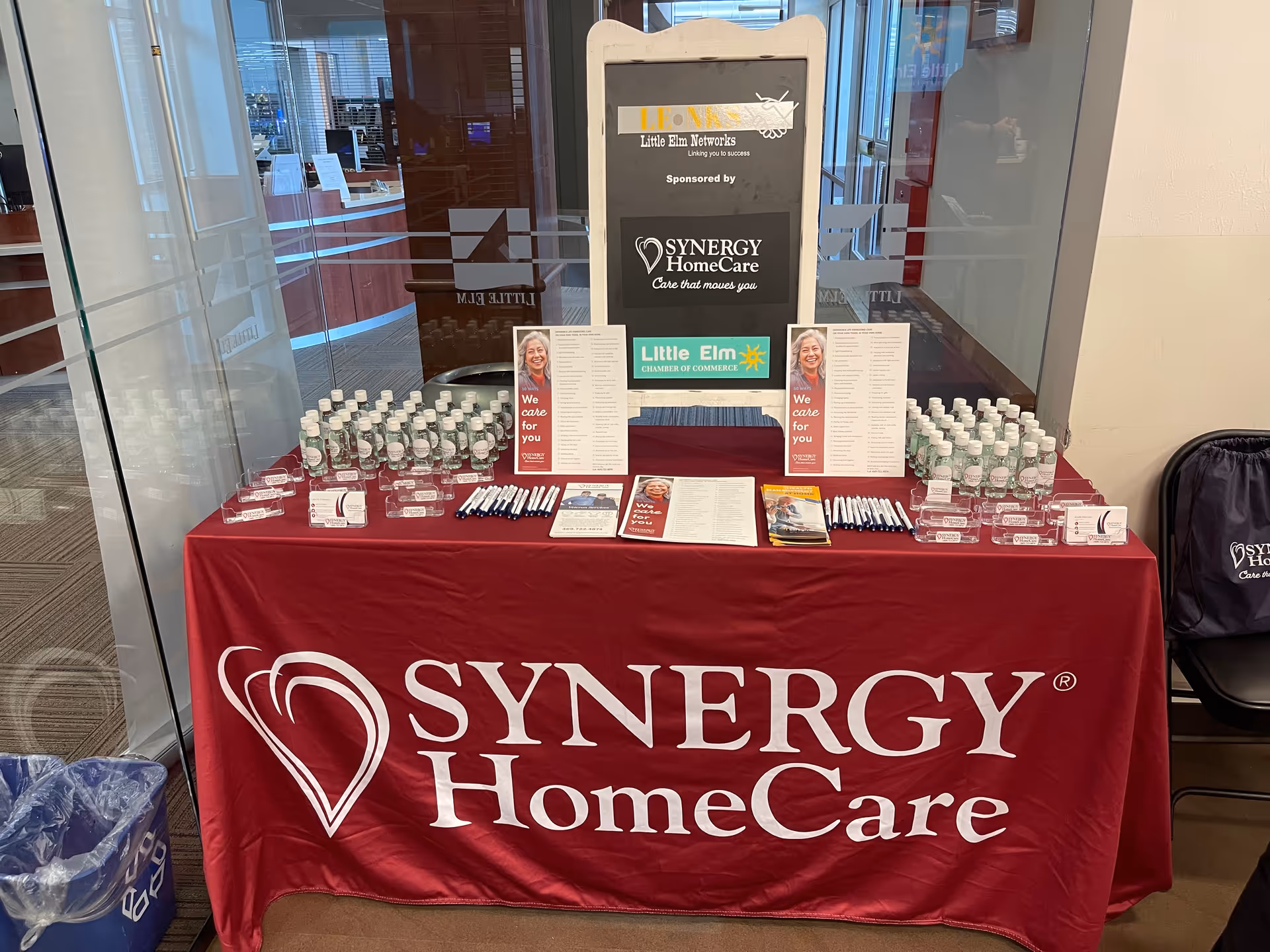 Promotional display table with SYNERGY HomeCare branding in an indoor lobby.