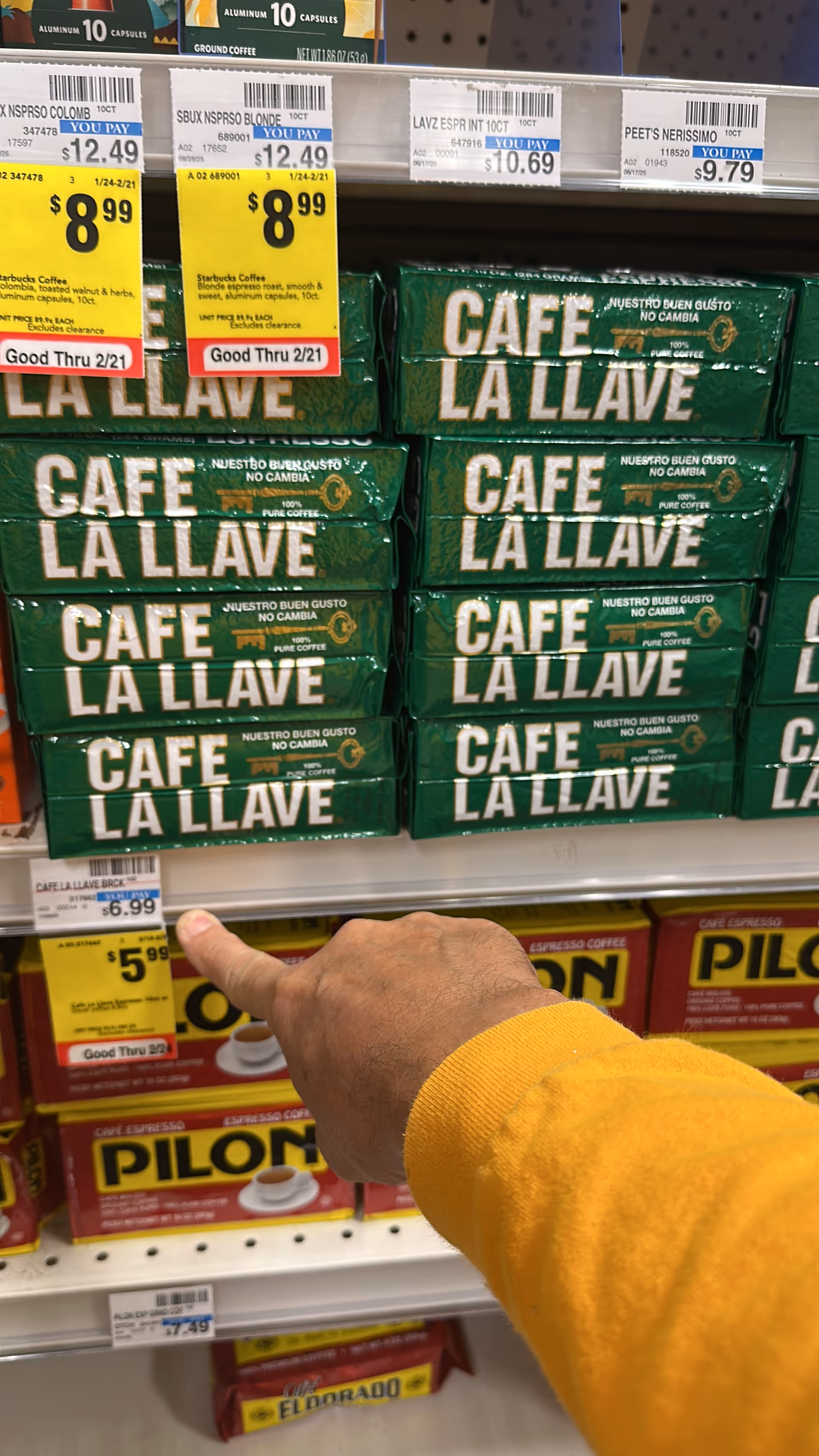 Close-up of green Café La Llave coffee boxes on store shelves with a pointing hand.