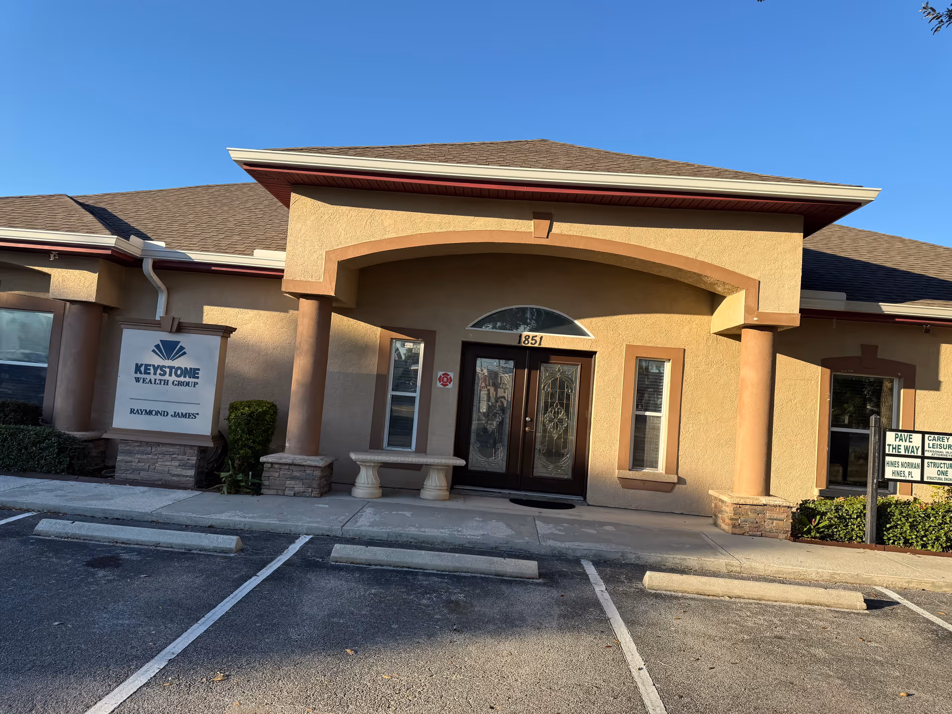 Beige building facade with an arched entrance, columns, and a front parking area.