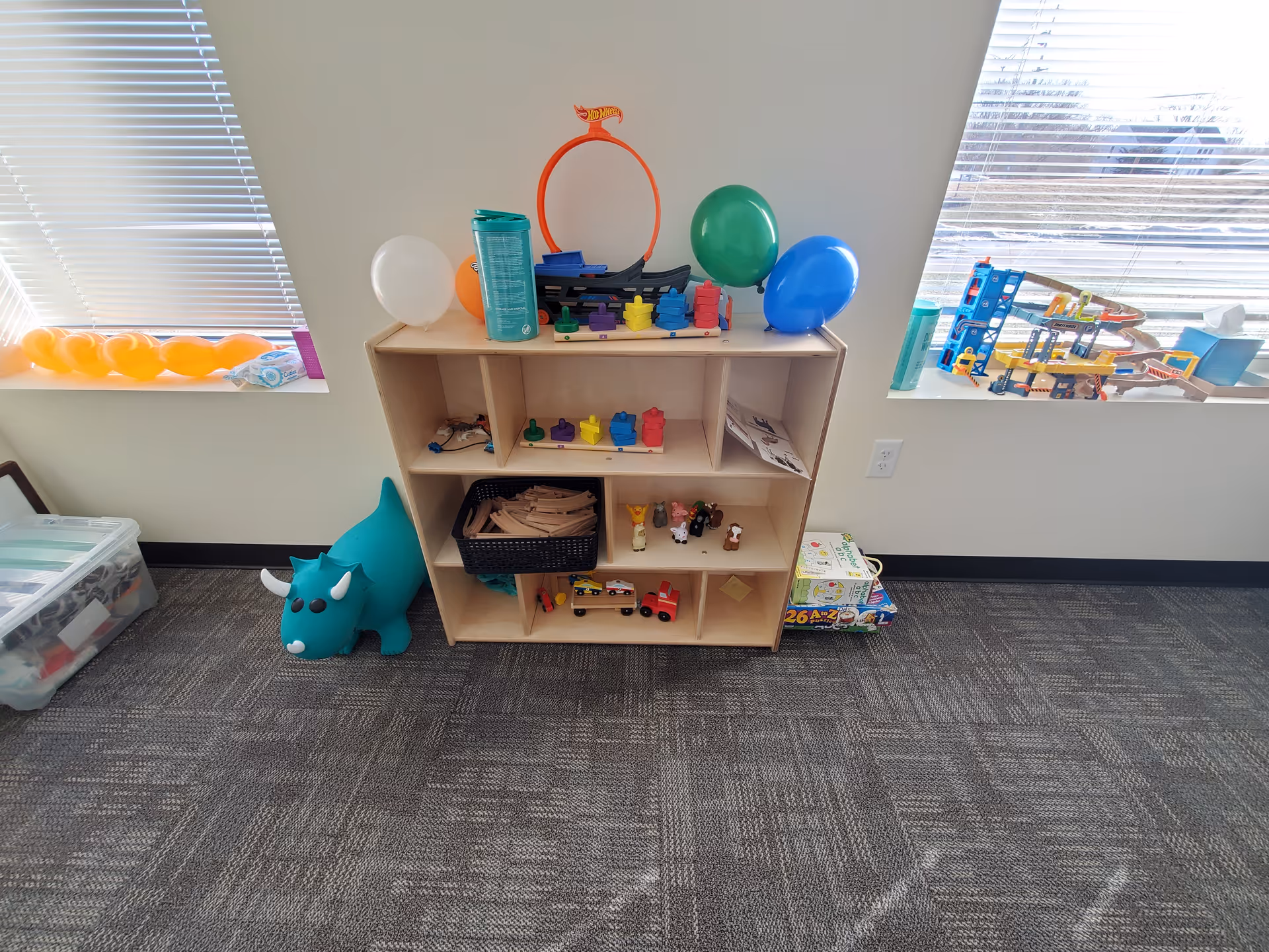 Toy shelves with balloons, assorted blocks, and a blue dinosaur in a bright play area.