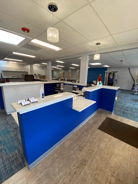Blue reception desk inside a rehab facility with gym equipment visible in background.