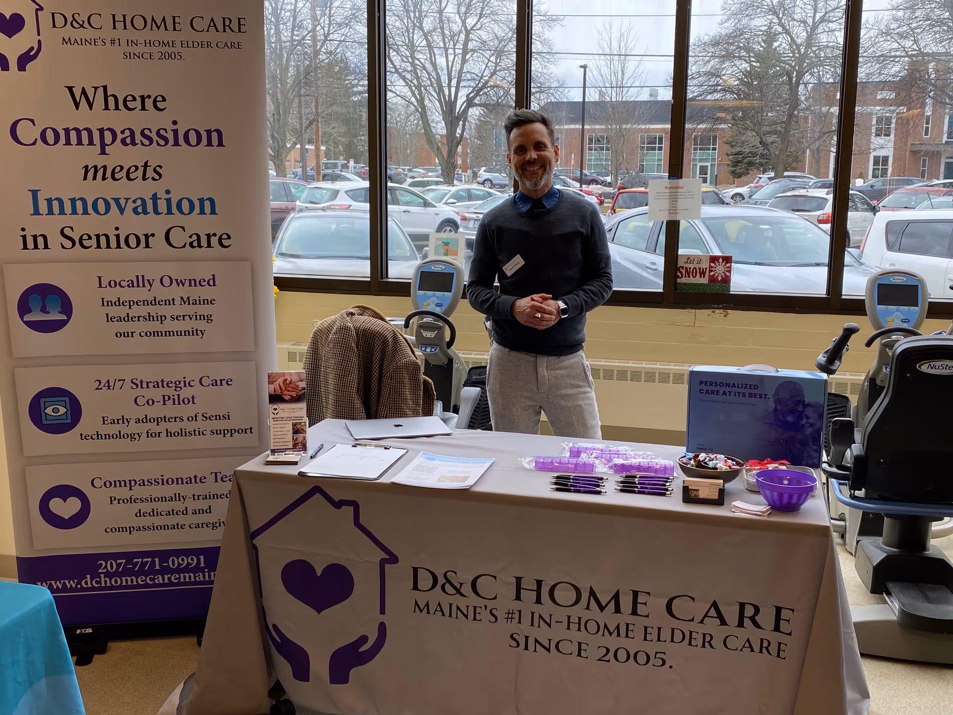 Man stands behind a promotional table inside a D&C Home Care booth in a lobby.