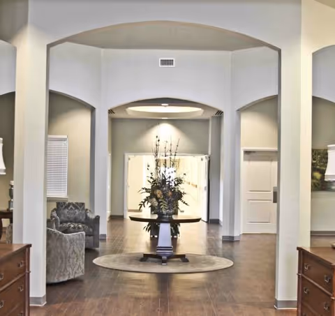 Interior lobby of Harbor Hospice Lake Charles with arched entrances and central flower arrangement.