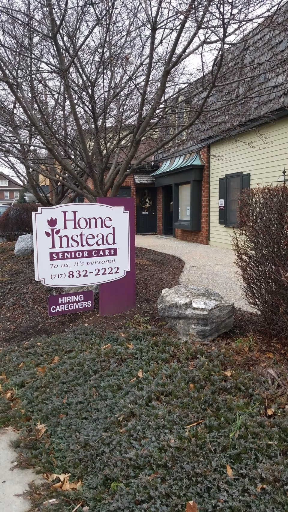 Exterior view of a Home Instead Senior Care building entrance with a purple sign and landscaping.
