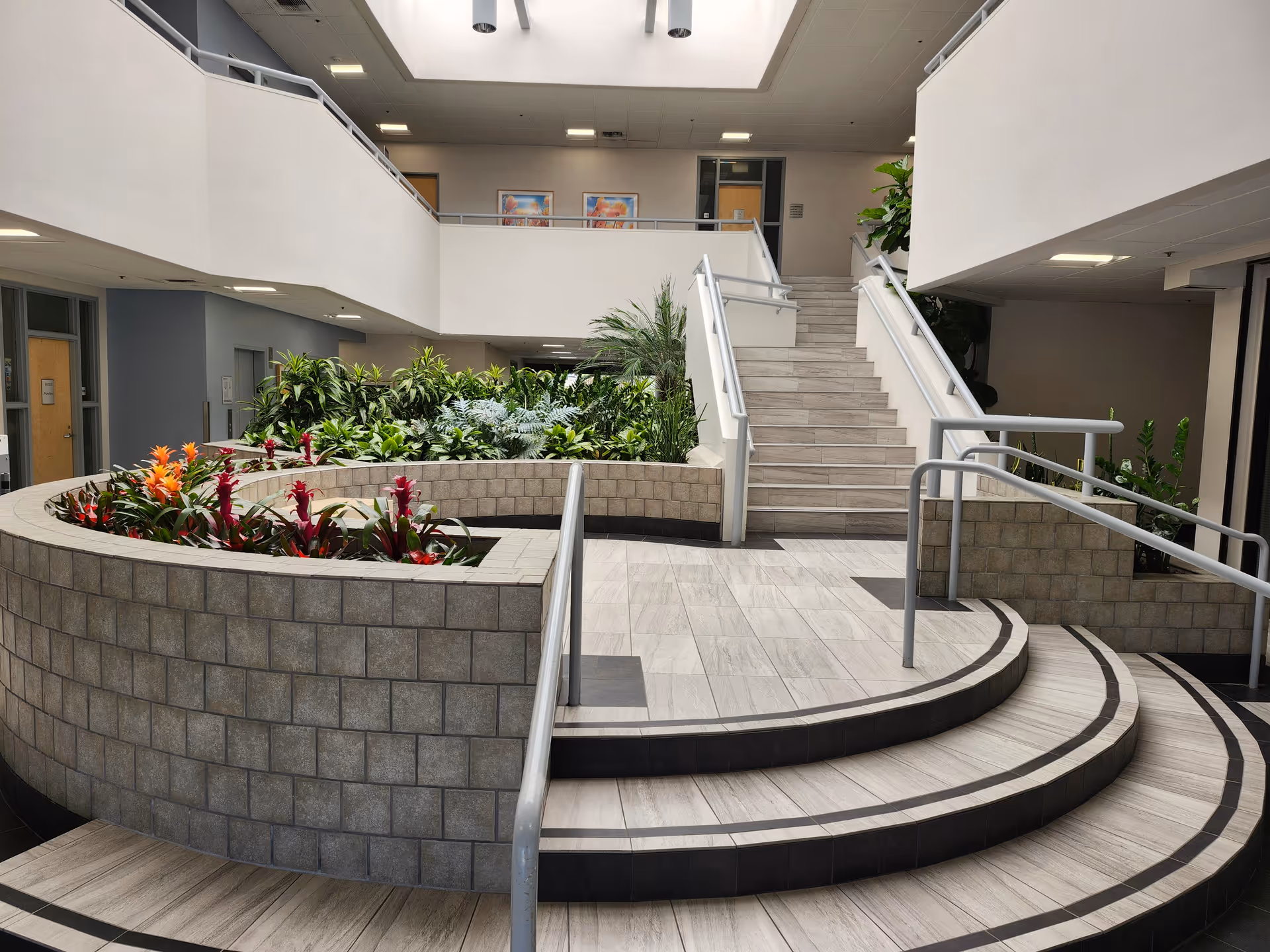 Interior atrium with curved planter, stairs, and lush plants in a modern senior care facility.