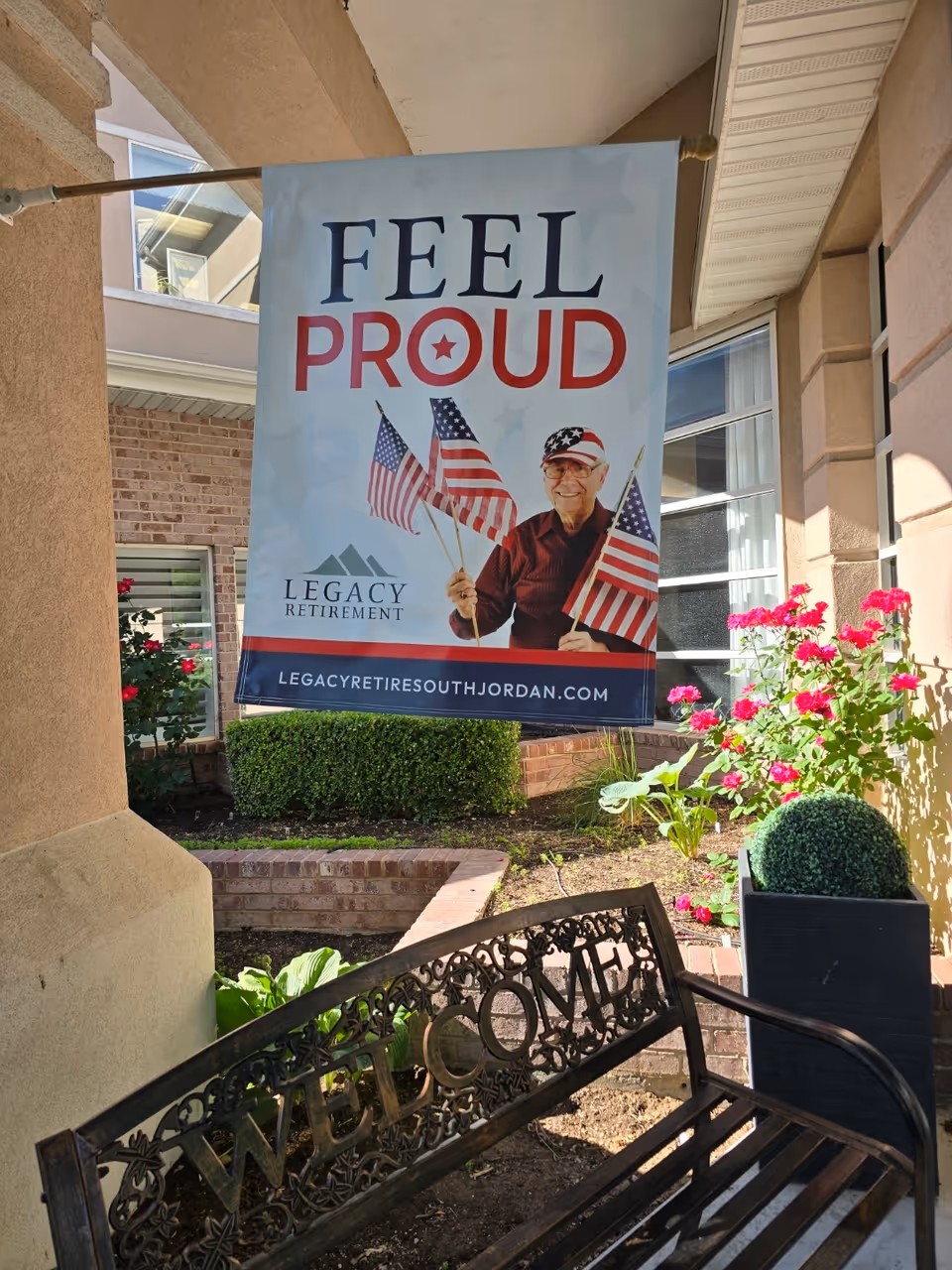 Outdoor entrance area with a large 'Feel Proud' banner and blooming flowers.