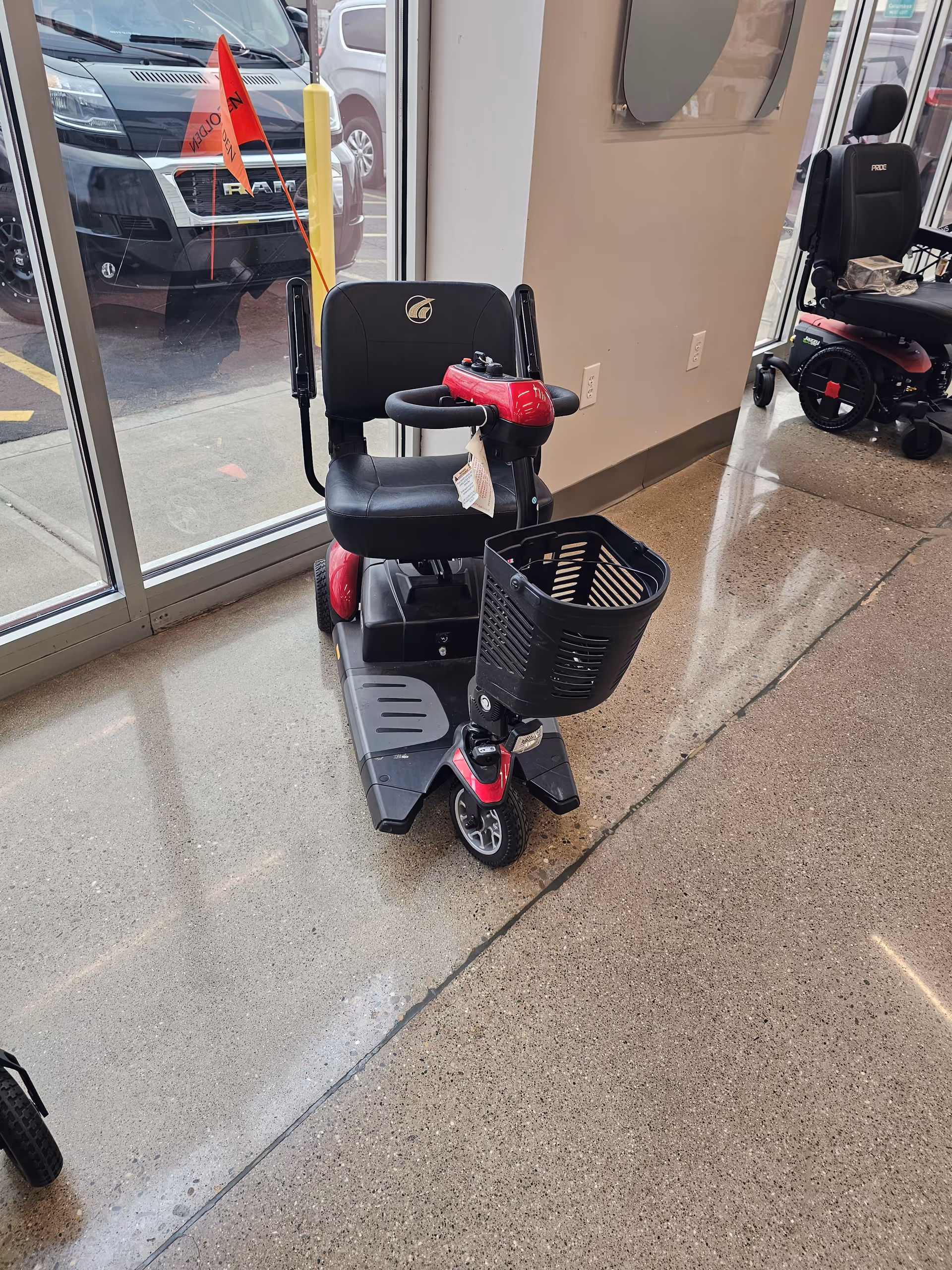 A mobility scooter with a front basket inside a showroom near large glass doors.