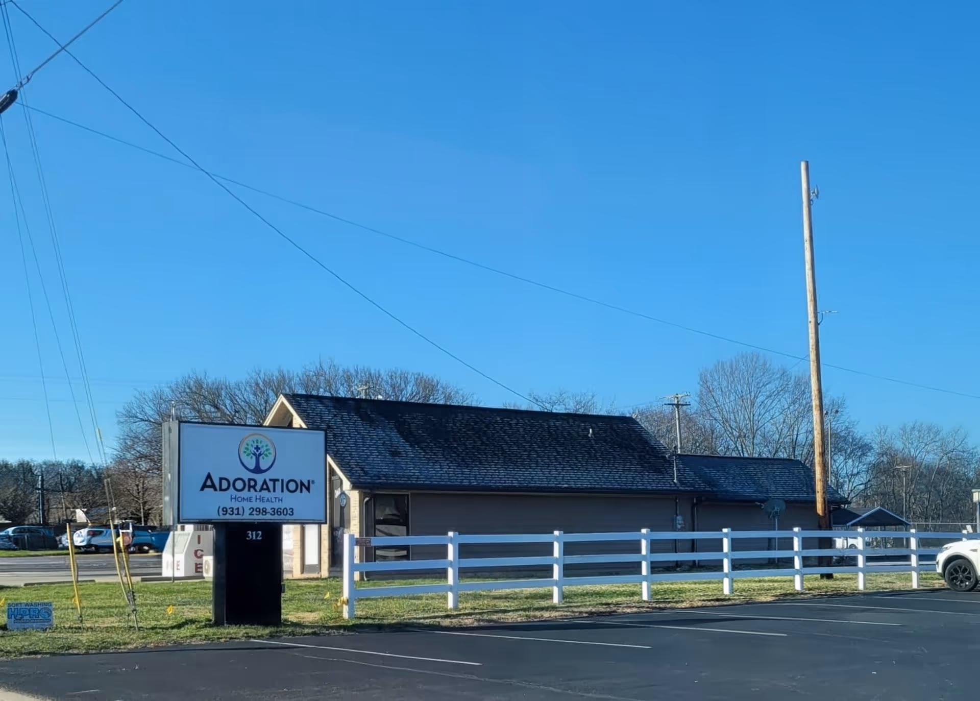 Exterior view of Adoration Home Health building with white fence and sign.
