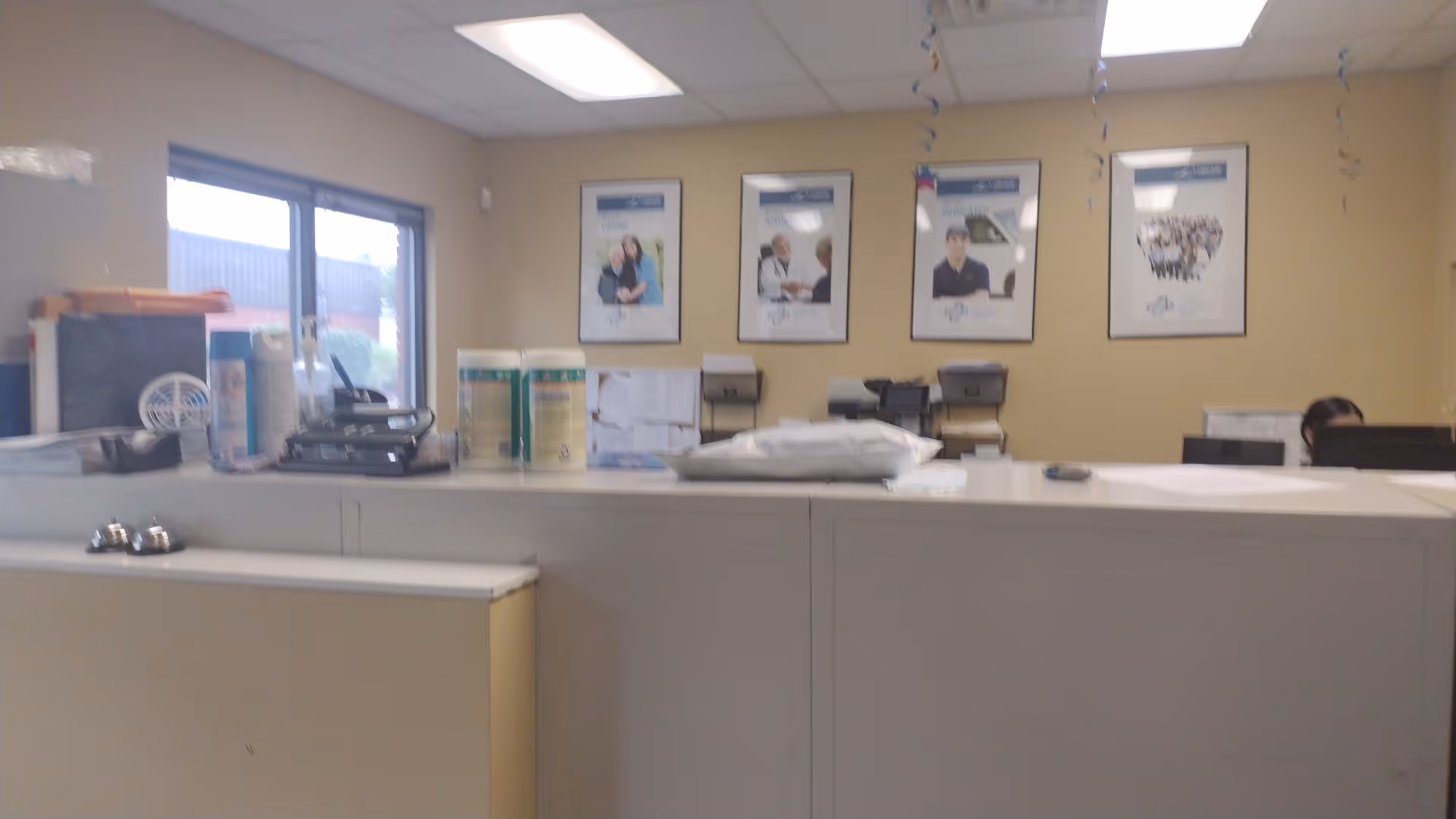 Reception area with a long counter, paperwork, and framed posters on beige walls.