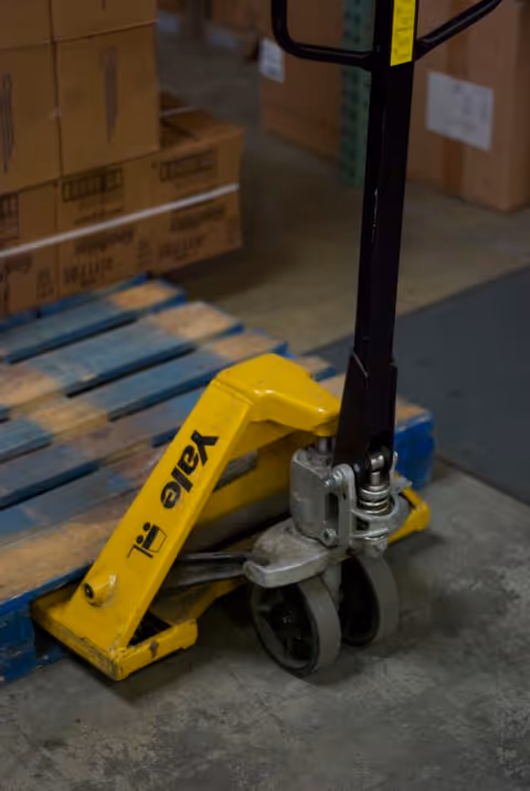 Yellow pallet jack beside stacked boxes in a warehouse storage area.
