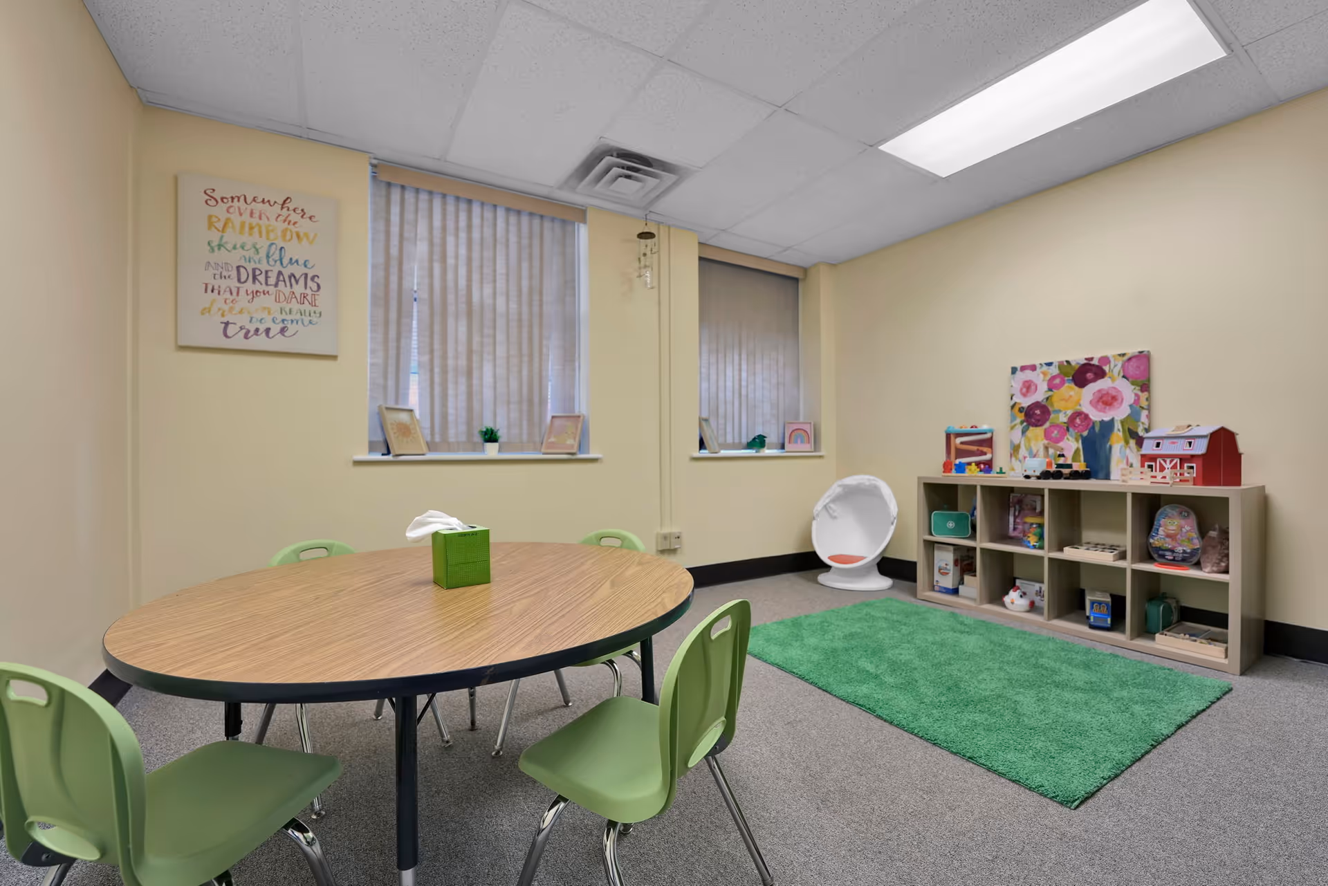 Interior activity room in a senior facility with a round table, green chairs, and cubby shelves.