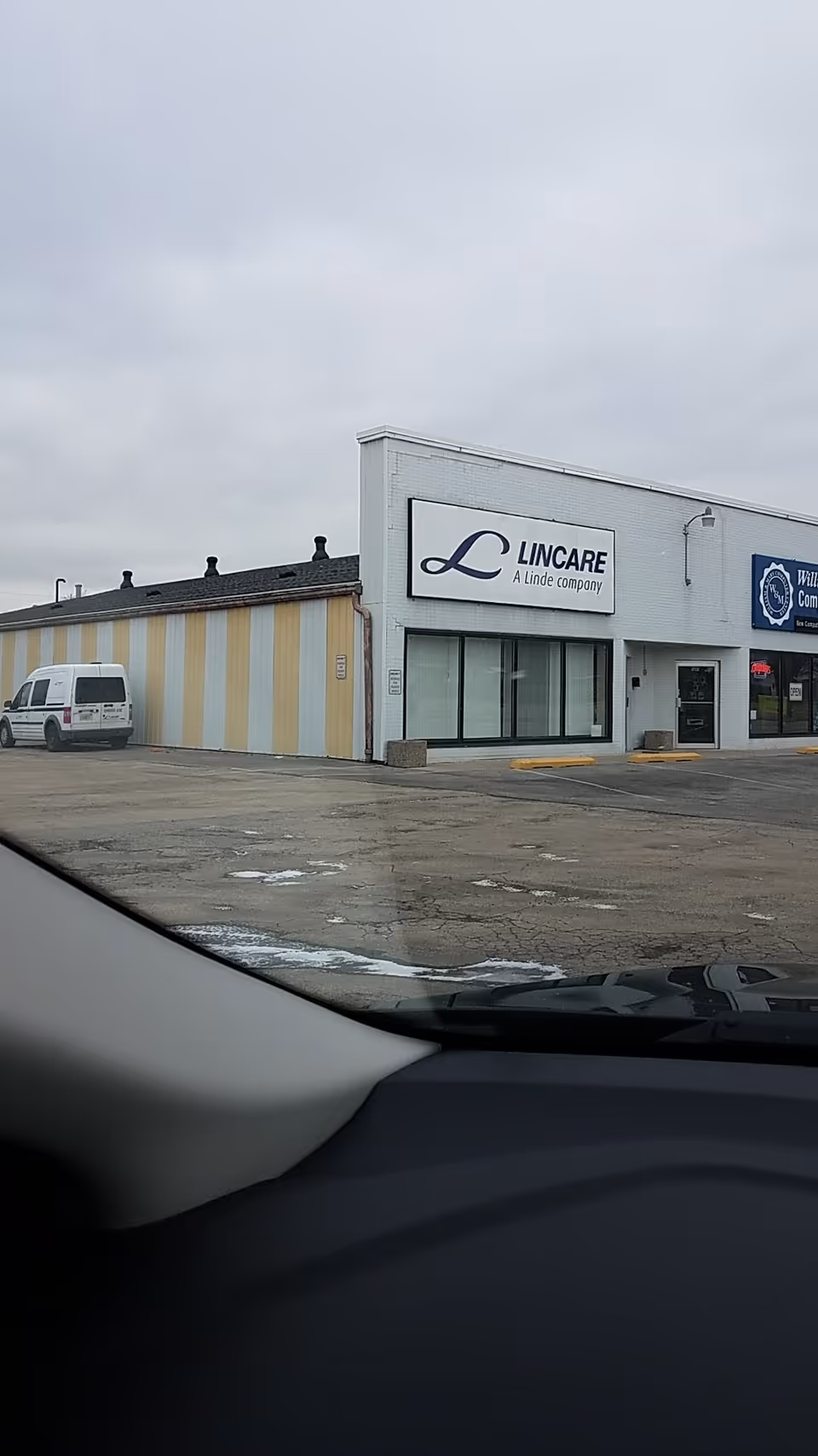 Exterior view of a LINCARE storefront with a striped annex and a parked white van.