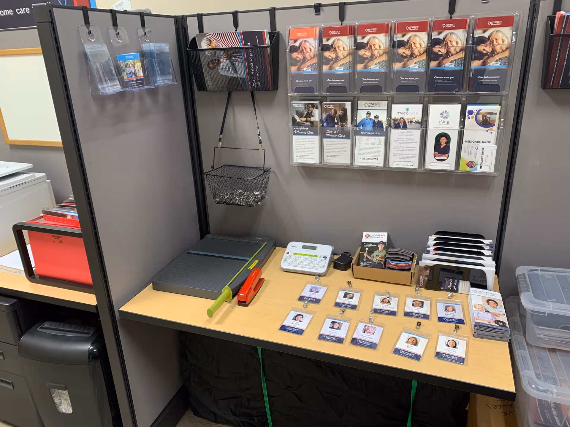 Office cubicle with brochures, badges, and desk supplies for SYNERGY HomeCare staff.