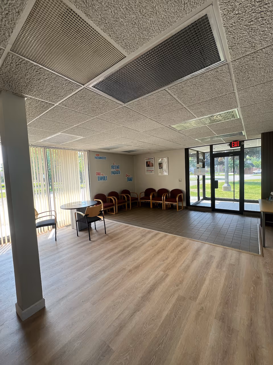 Interior waiting area with chairs along wall, glass doors, round table, and tiled entrance.