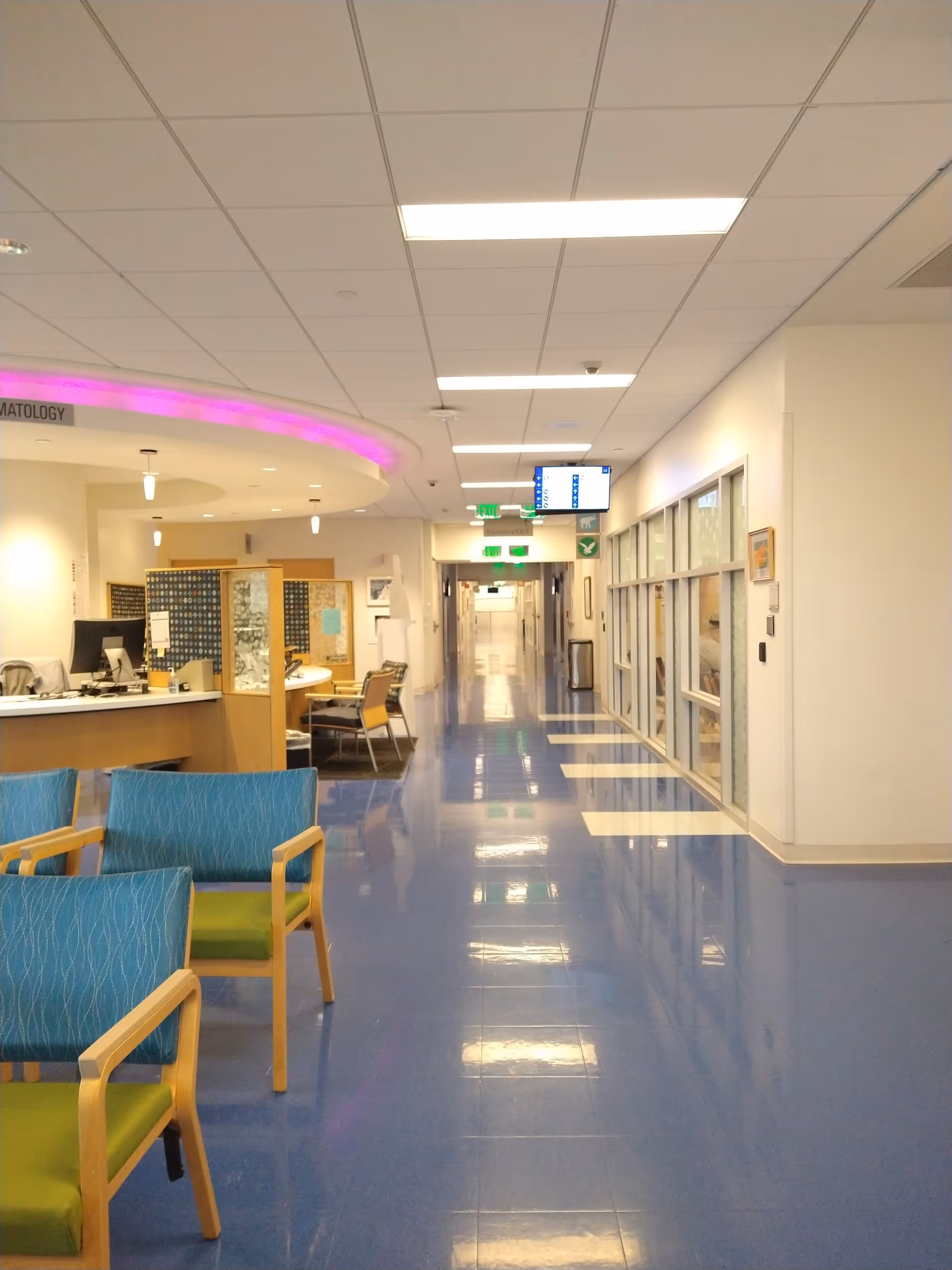 Bright hospital hallway with reception desk, blue floor tiles, and seating area.