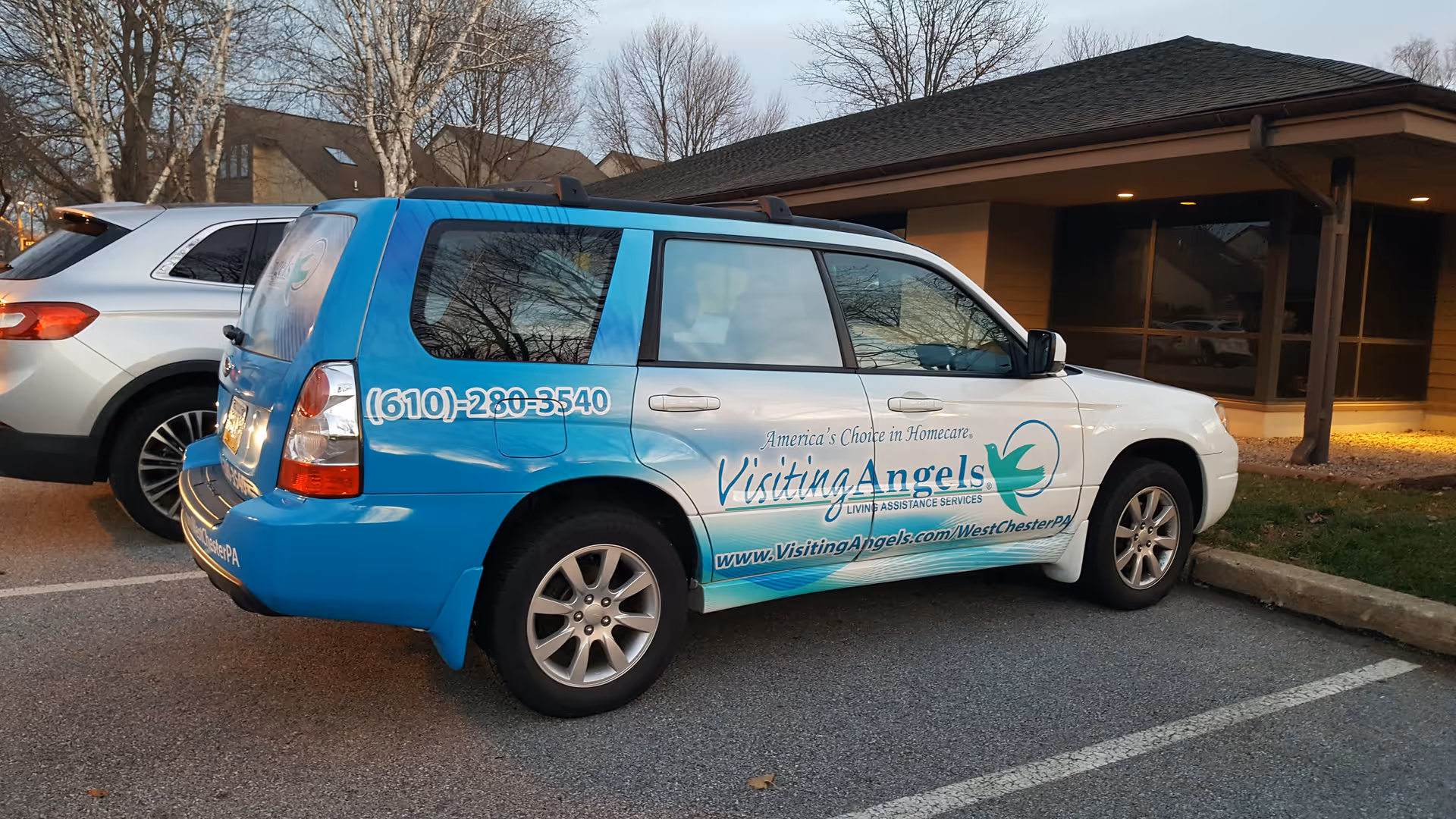 Blue and white Visiting Angels home care van parked in front of a facility.