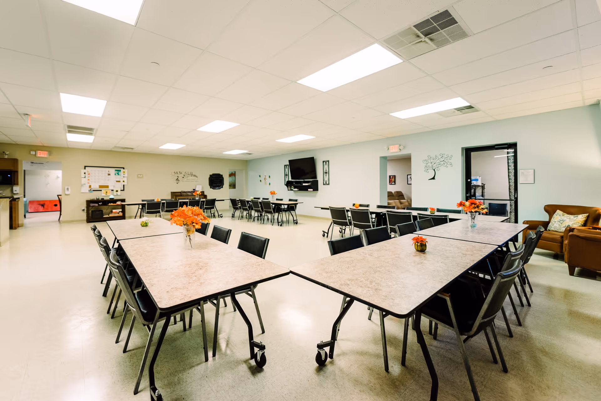 Large communal dining area with long tables, chairs, centerpieces, and a wall-mounted TV.