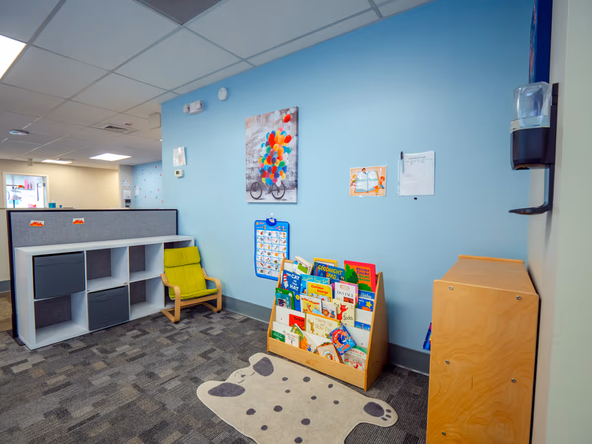 Bright blue wall with a book rack, cubbies, and a yellow chair in a reading corner.