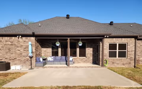 Brick exterior of Austin Senior Living with a shaded patio, seating, and hanging planters.