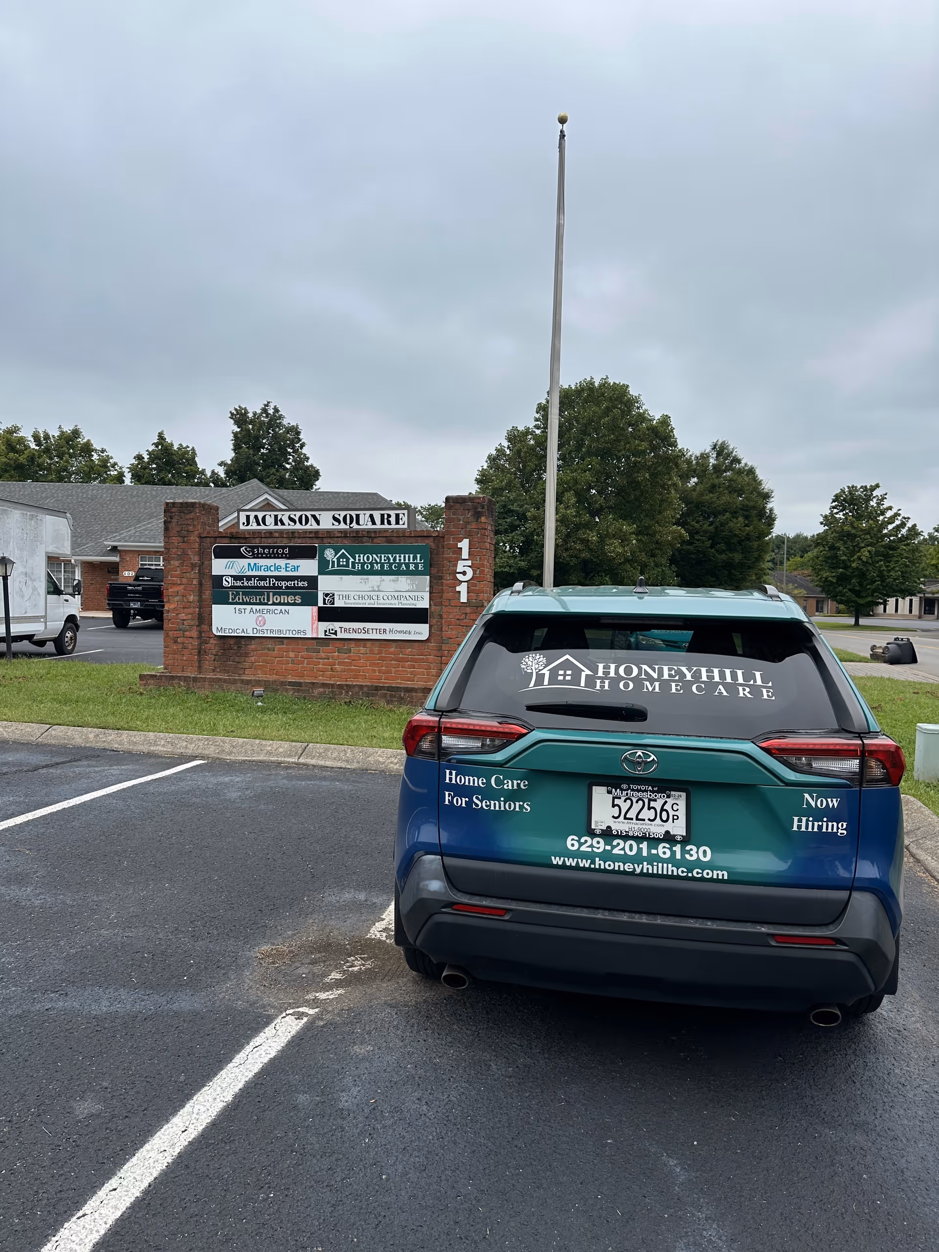Blue HoneyHill HomeCare vehicle parked near Jackson Square sign at the facility.