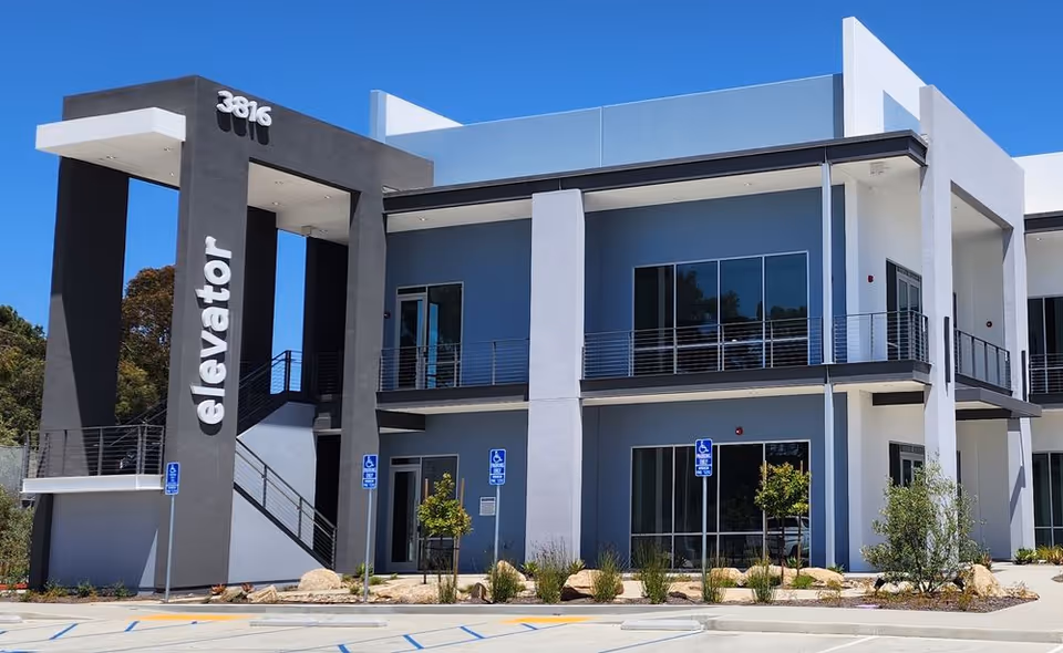 Modern two-story senior living building exterior with elevator sign and accessible parking.
